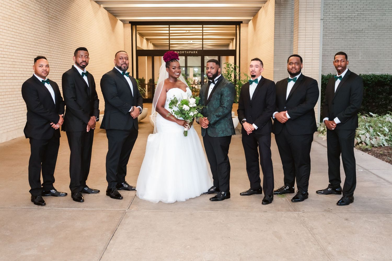 Formal wedding party portrait with groomsmen in black suits and white bouquet.