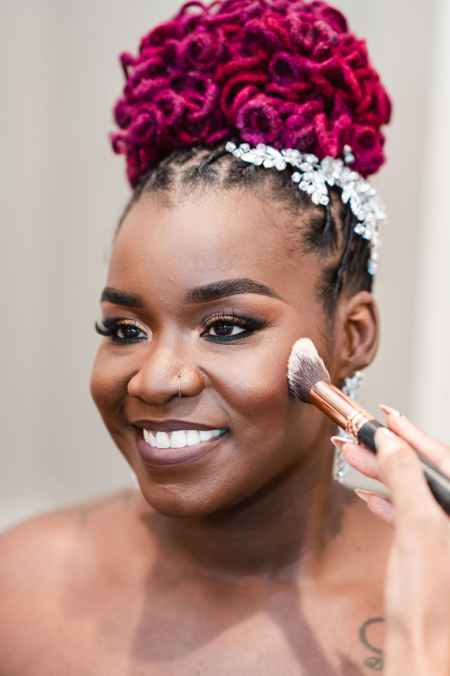 Wedding makeup application showing bright magenta hair and silver accessories.