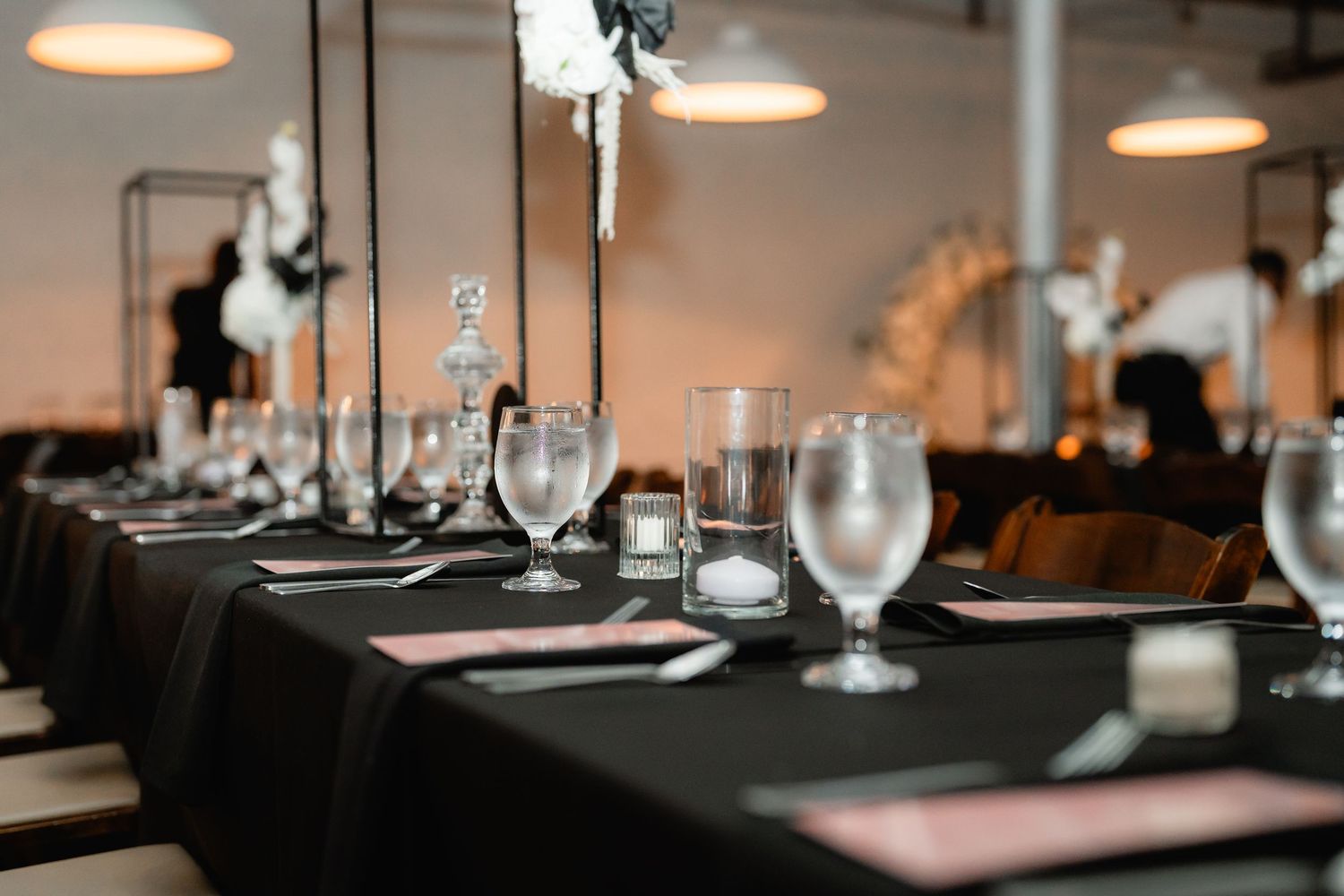 Place settings and glassware arranged on tables at an elegant indoor wedding reception.