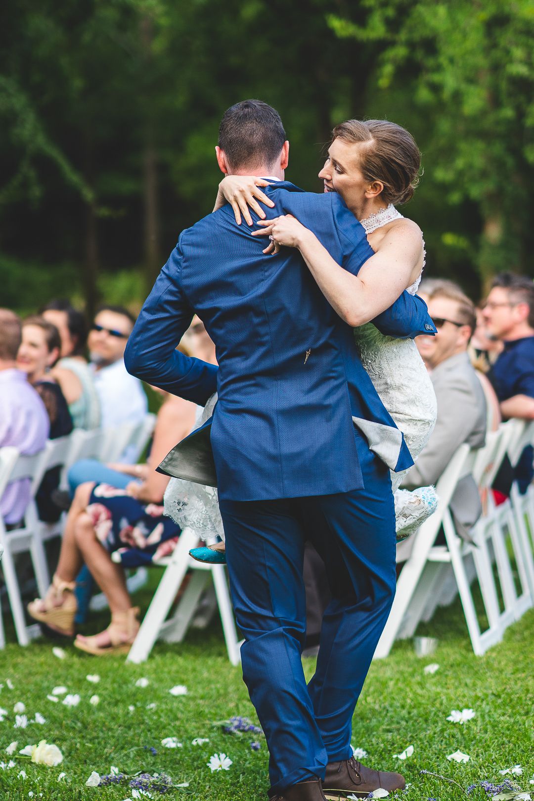 Wedding couple performs first dance surrounded by guests seated on white chairs outdoors.