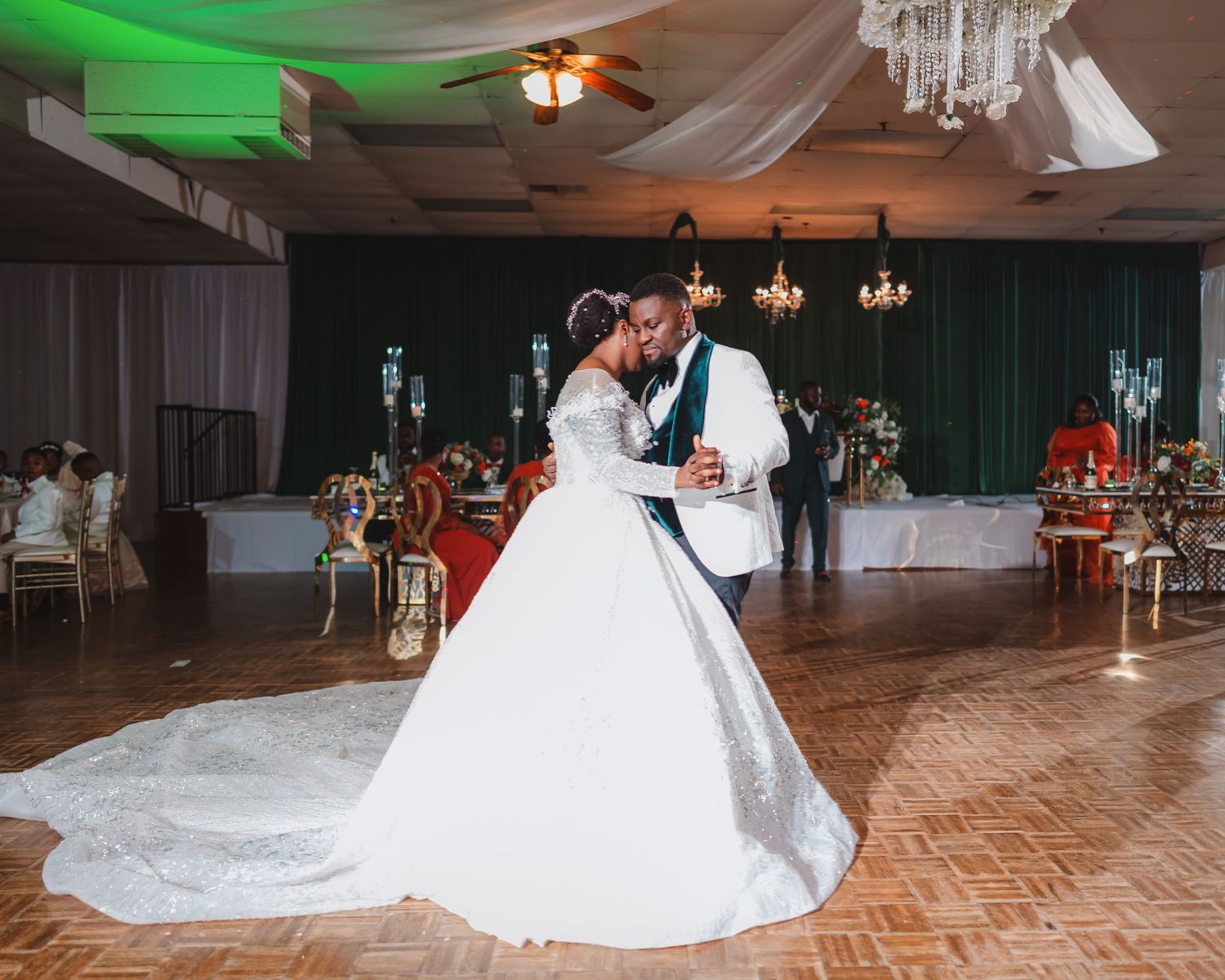Wedding reception venue with elegant chandeliers, draped white fabric, and a wooden dance floor.