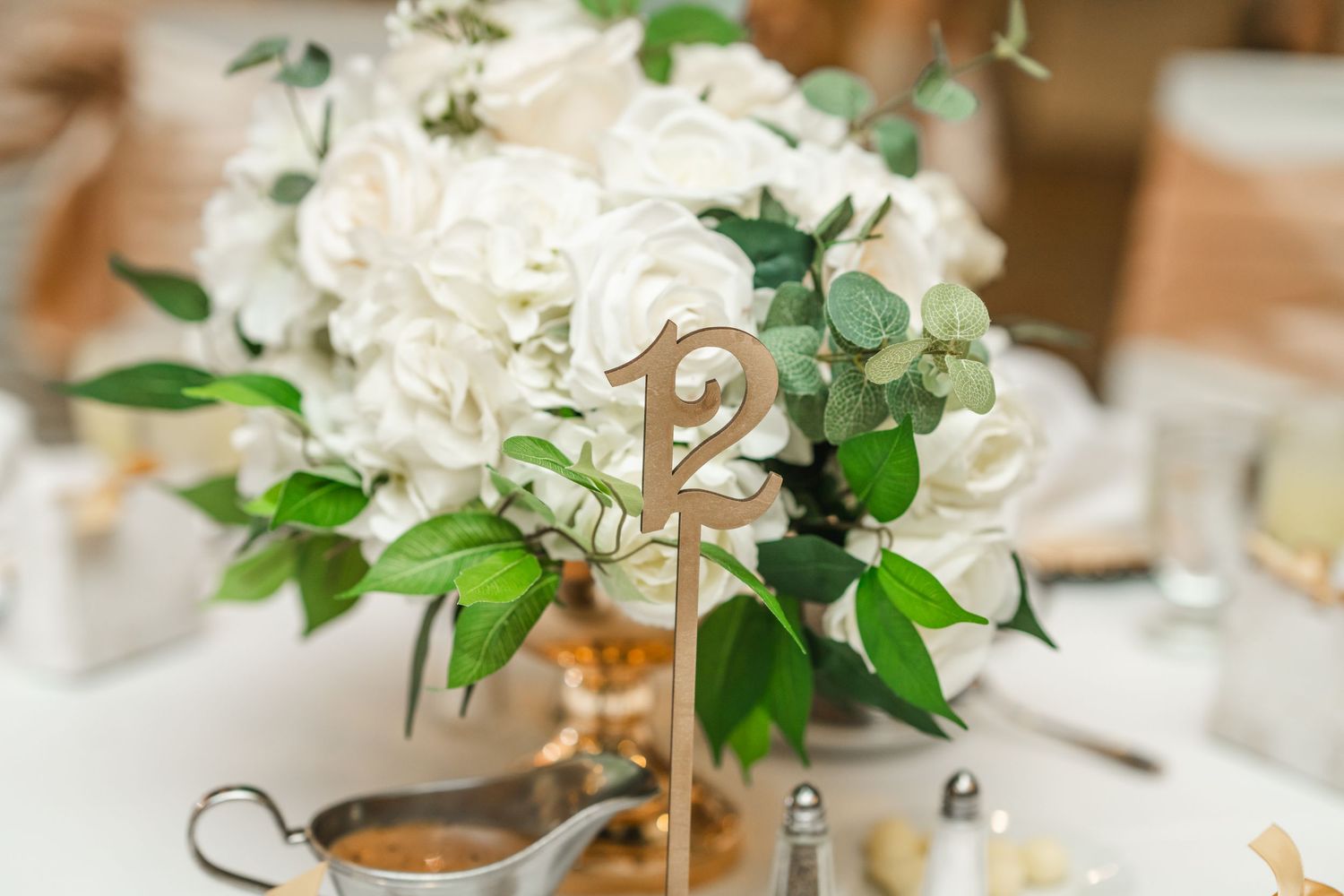 White floral centerpieces with green foliage arranged on wedding reception tables.