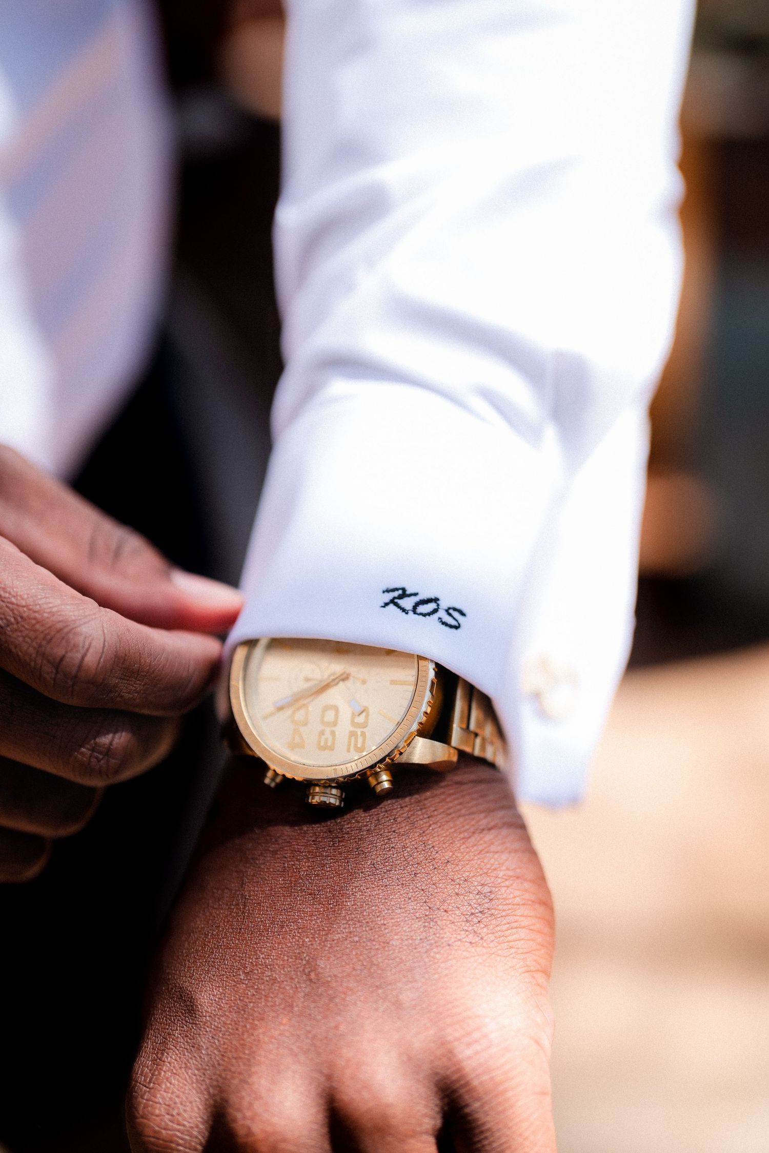 Close-up of monogrammed shirt cuff with 'KDS' initials and gold watch detail.