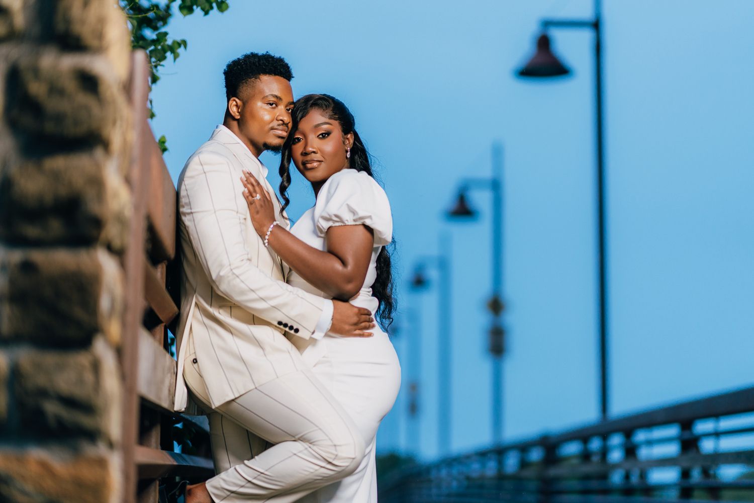 A couple shares an intimate dance pose on a boardwalk with lampposts in the background.