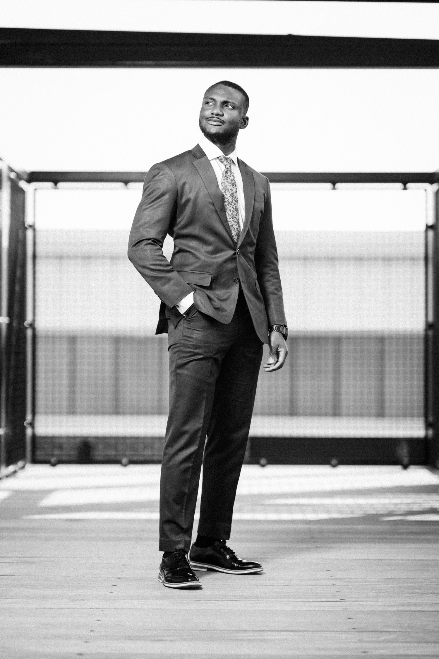 Man in gray suit walking and posing in modern architectural setting with black and white filter.