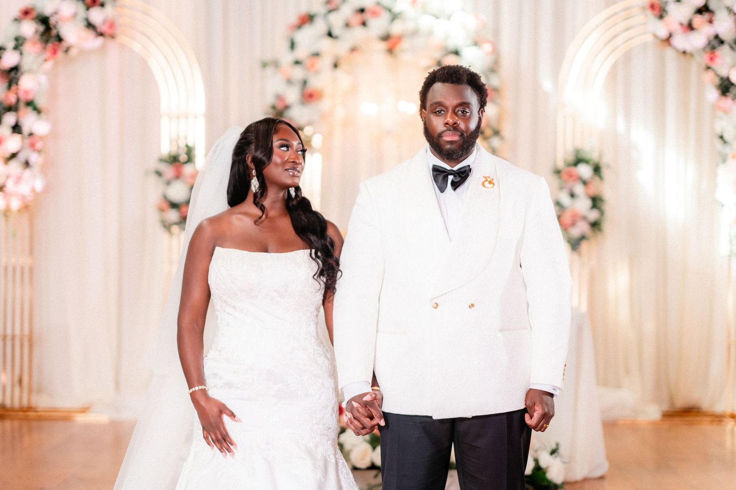 Wedding couple dancing and celebrating in an elegant white-decorated reception hall.