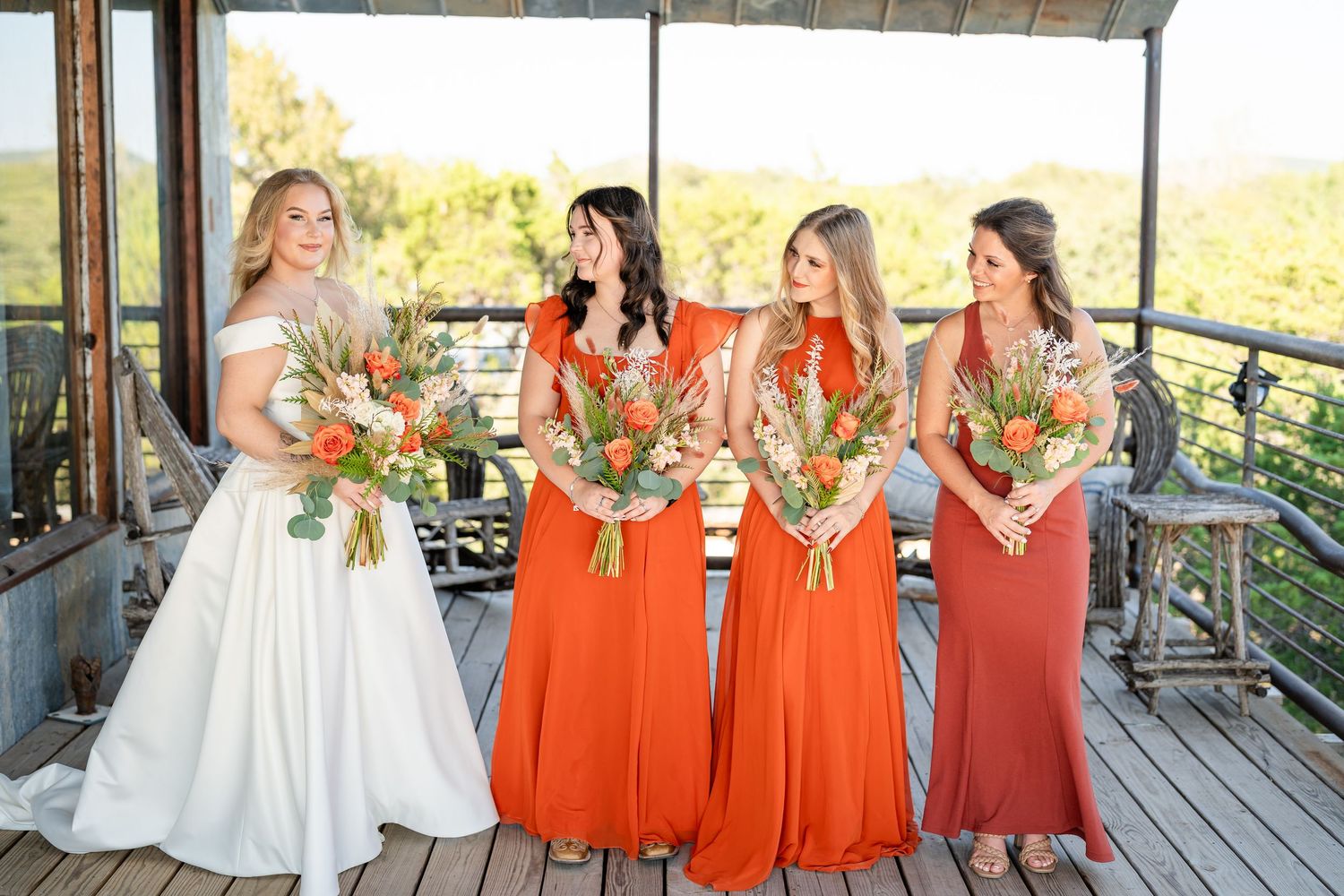 Bridesmaids in coral dresses posing together on covered outdoor deck.