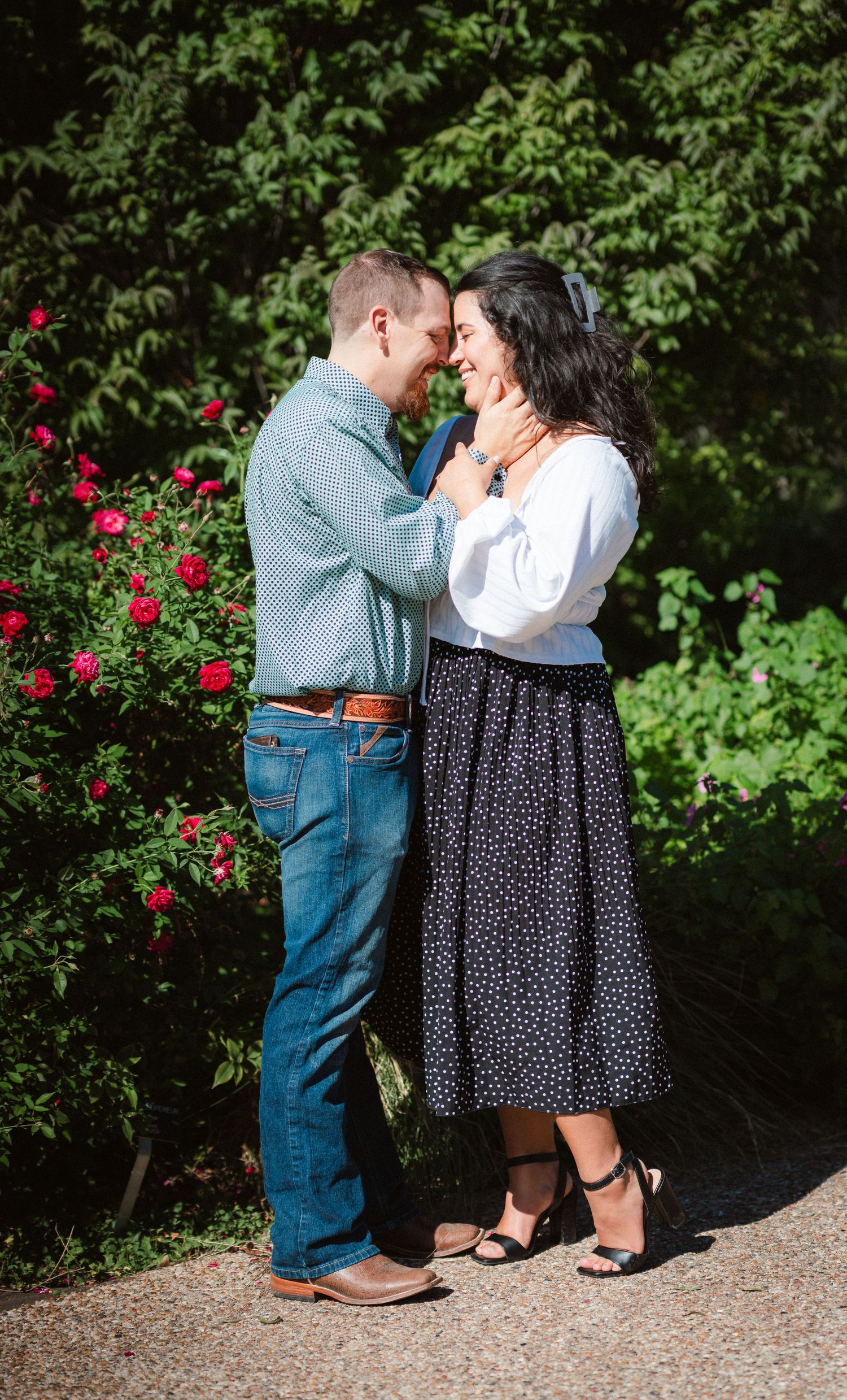A romantic moment shared between a couple in a garden with blooming red roses in the background.