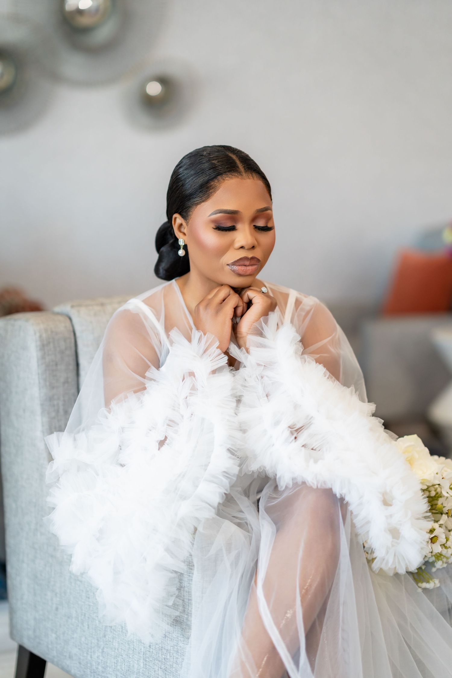 Person wearing a white tulle robe with feather details while sitting in a grey chair.
