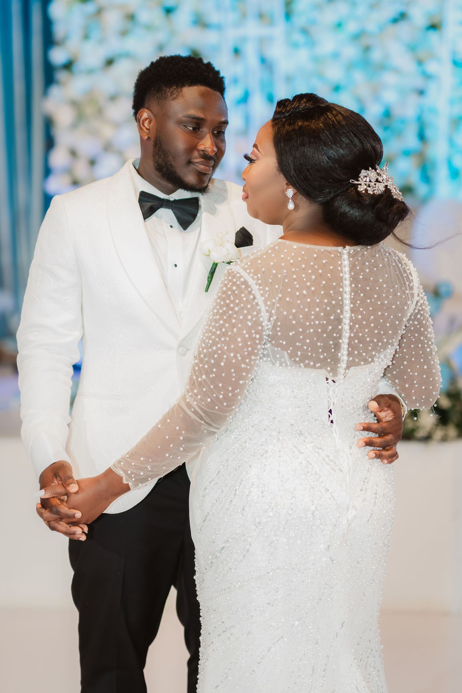 A newlywed couple dances together in an elegant ballroom with blue lighting and floral decor.