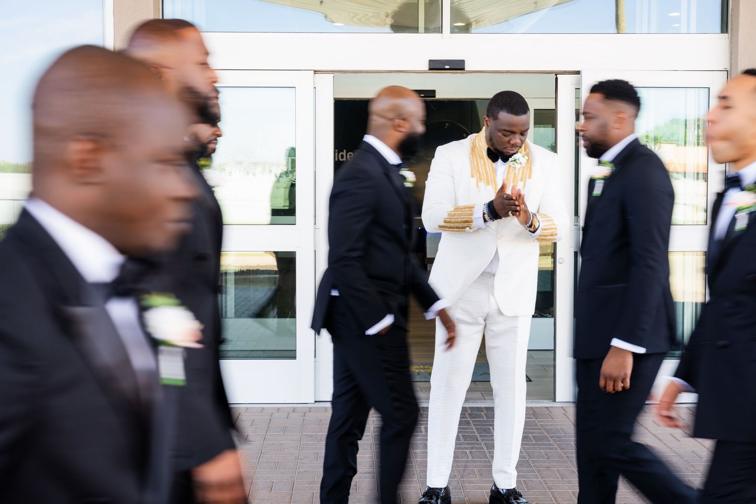 Wedding party in formal attire walking and posing outside glass building entrance.