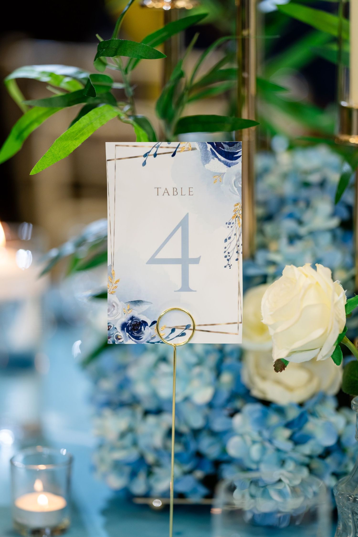 Elegant wedding table numbers 1 and 4 displayed with white roses and blue hydrangeas in soft focus lighting.
