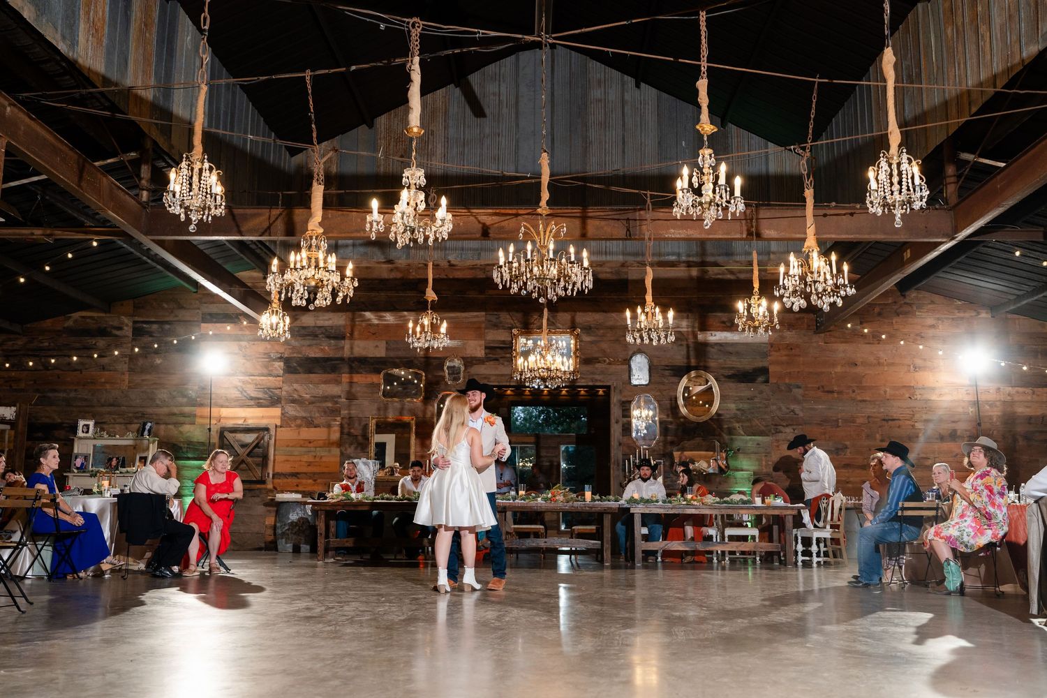 Panoramic shot of a rustic barn reception venue decorated with multiple crystal chandeliers.