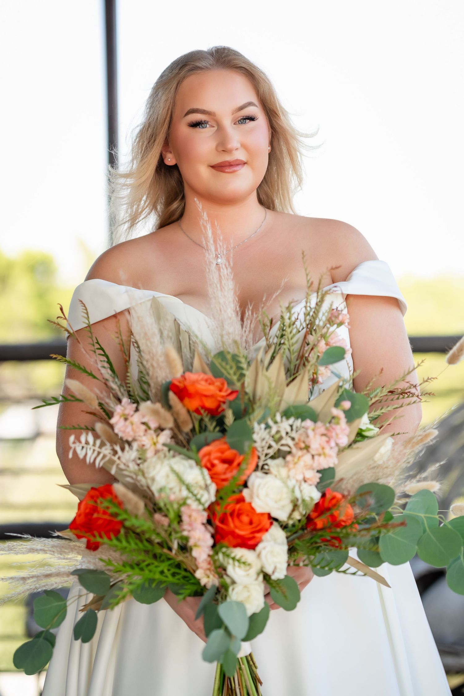 Beautiful bridal bouquet with orange roses and mixed greenery against natural light.