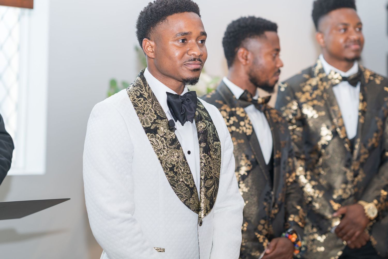 Wedding party members in elegant black and white attire with gold accents pose together.