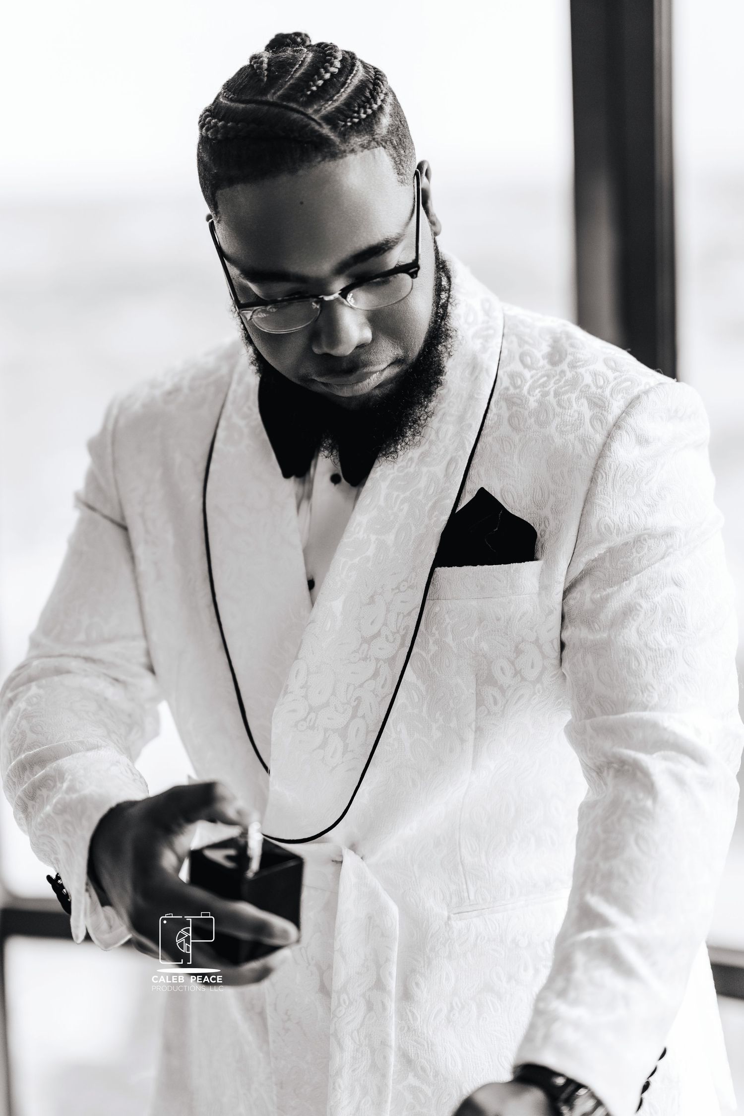 A groom in a white textured tuxedo jacket and bow tie looks down while adjusting his cuffs.
