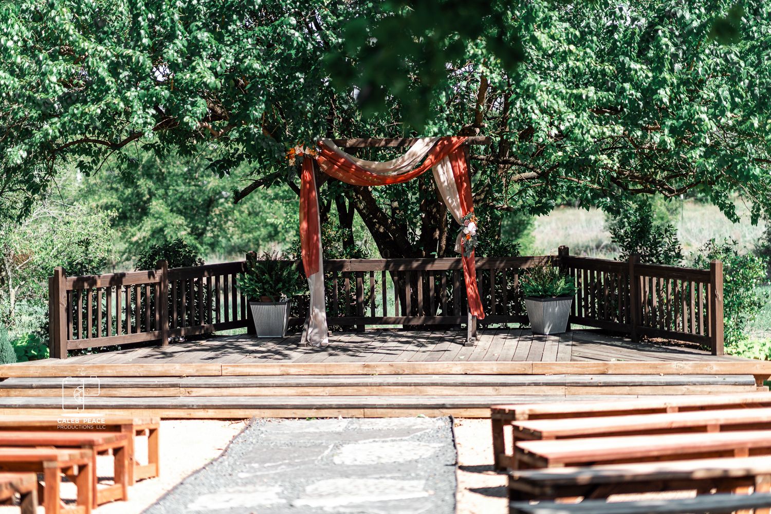 Outdoor wedding ceremony setup with wooden benches and natural greenery creating an aisle.