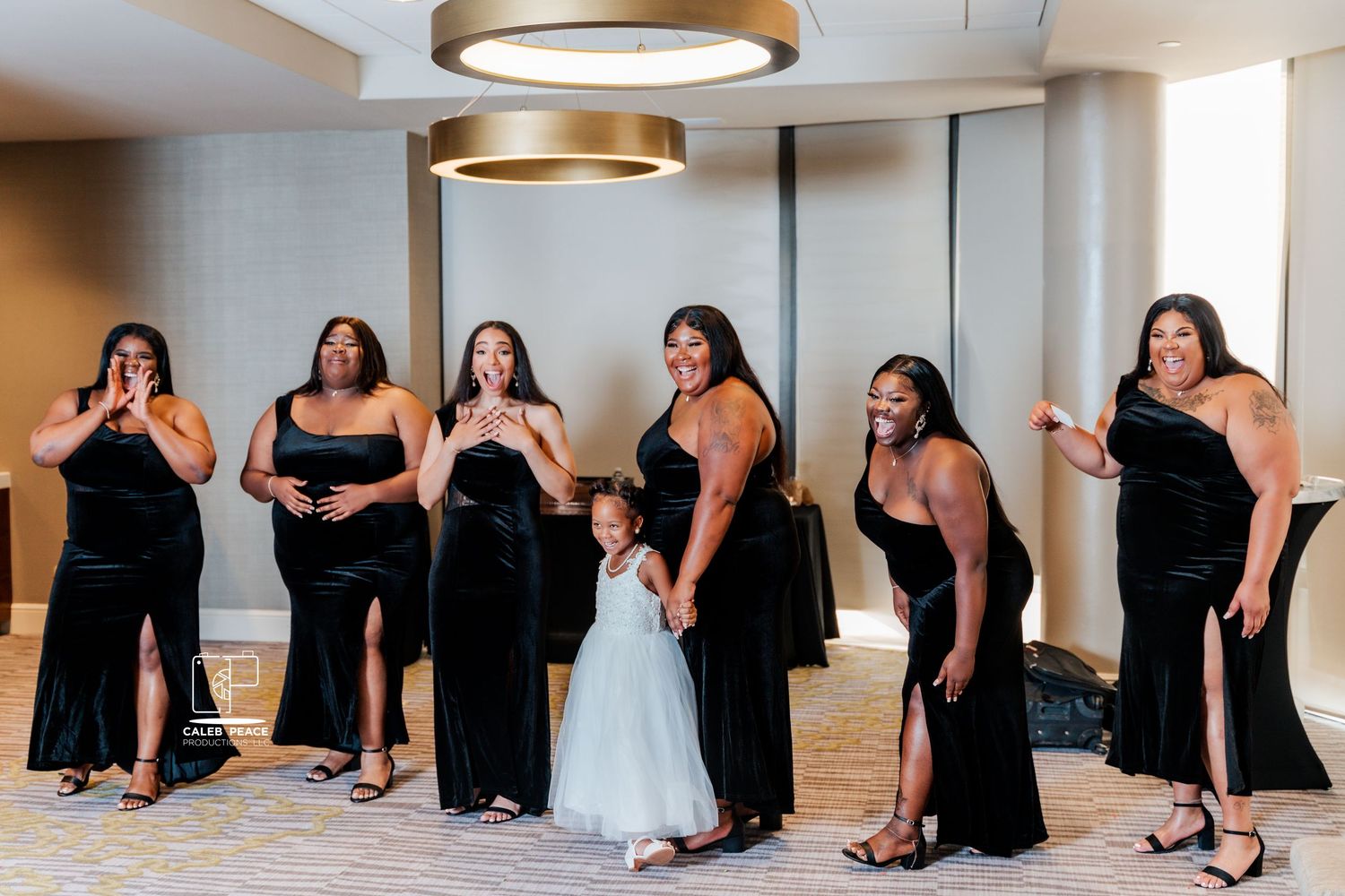 A bridal party in black dresses poses with a flower girl in white.
