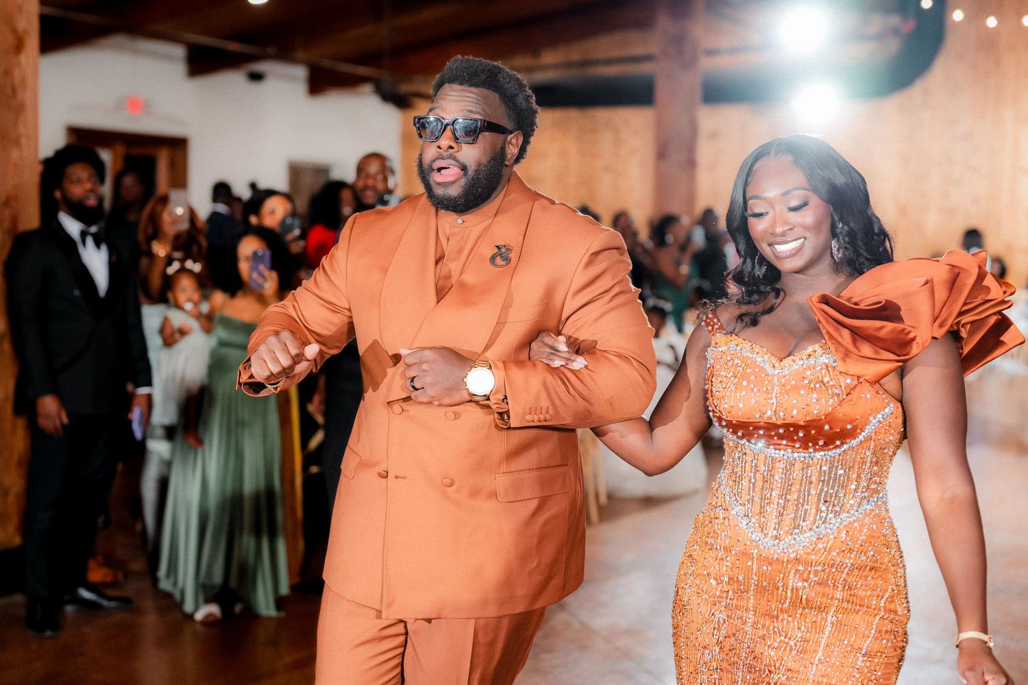 Wedding reception guests in orange attire dancing and celebrating in an indoor venue.