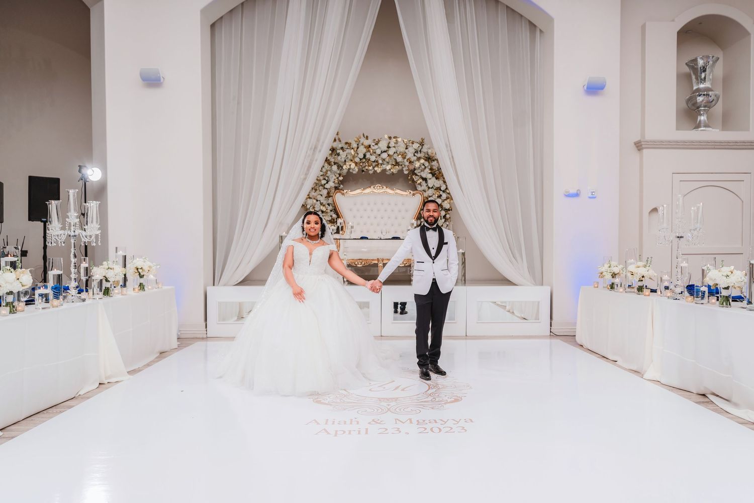 Elegant white ballroom decorated for wedding reception with draped ceiling and soft lighting.