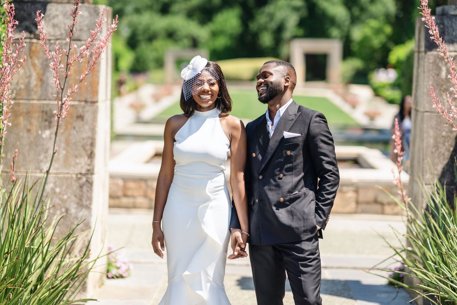 Wedding couple poses in an elegant outdoor garden setting with stone pillars and landscaping.