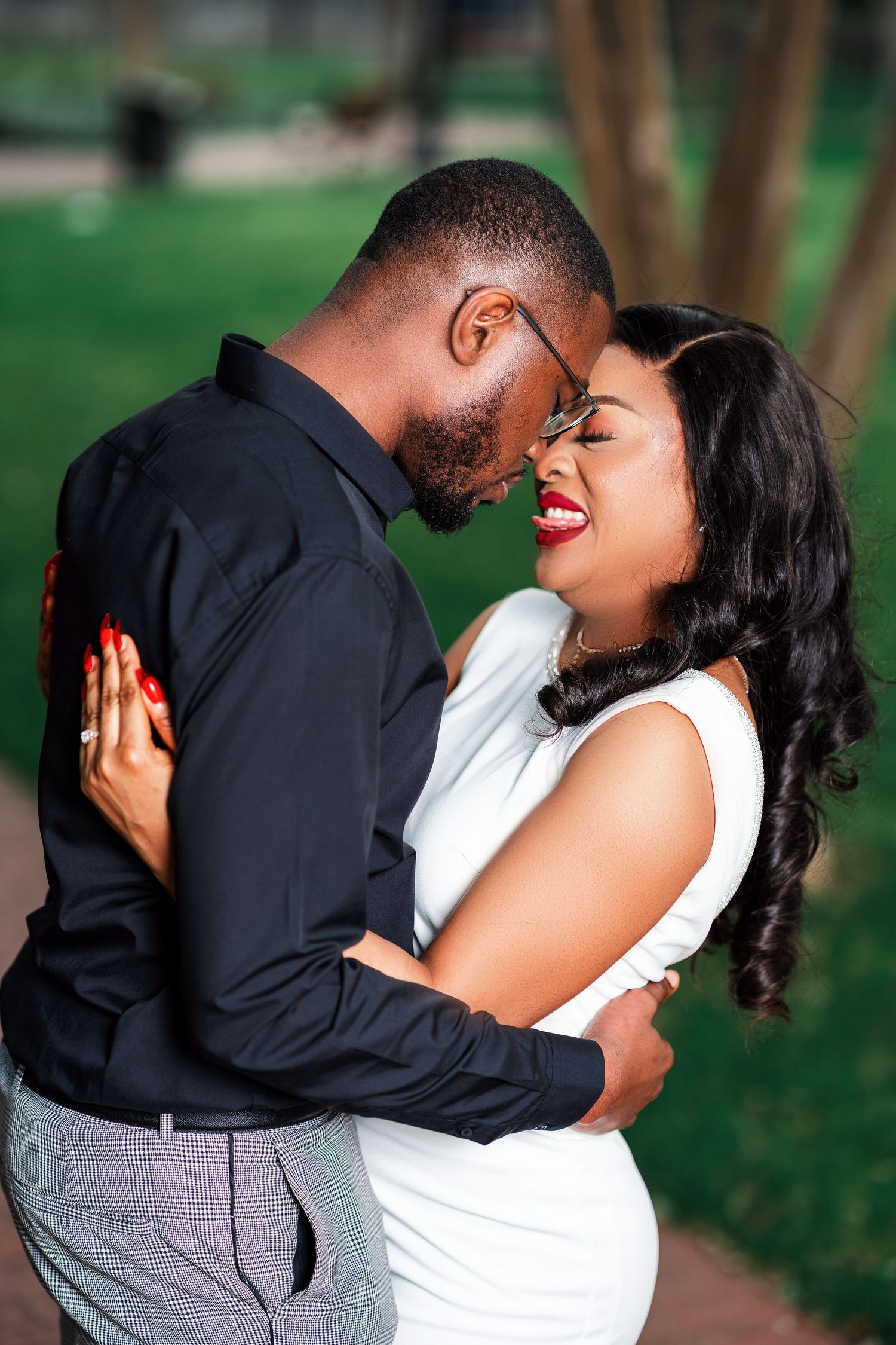 A romantic couple in formal attire share an intimate moment in a park setting.