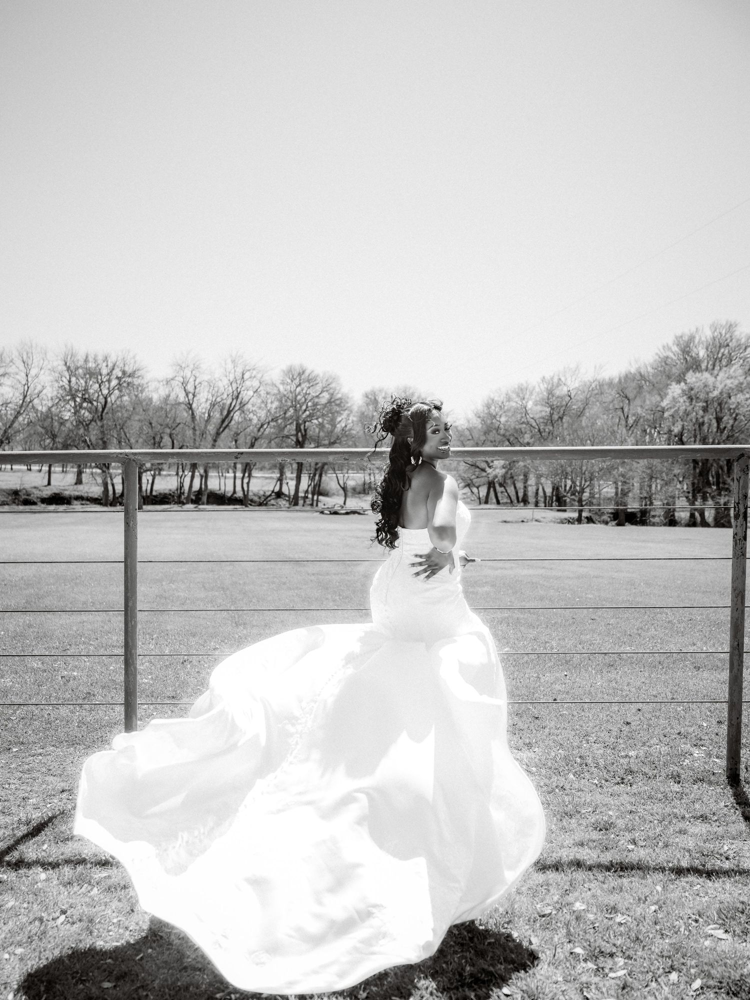 A flowing white wedding dress billows dramatically in the wind across an open field.