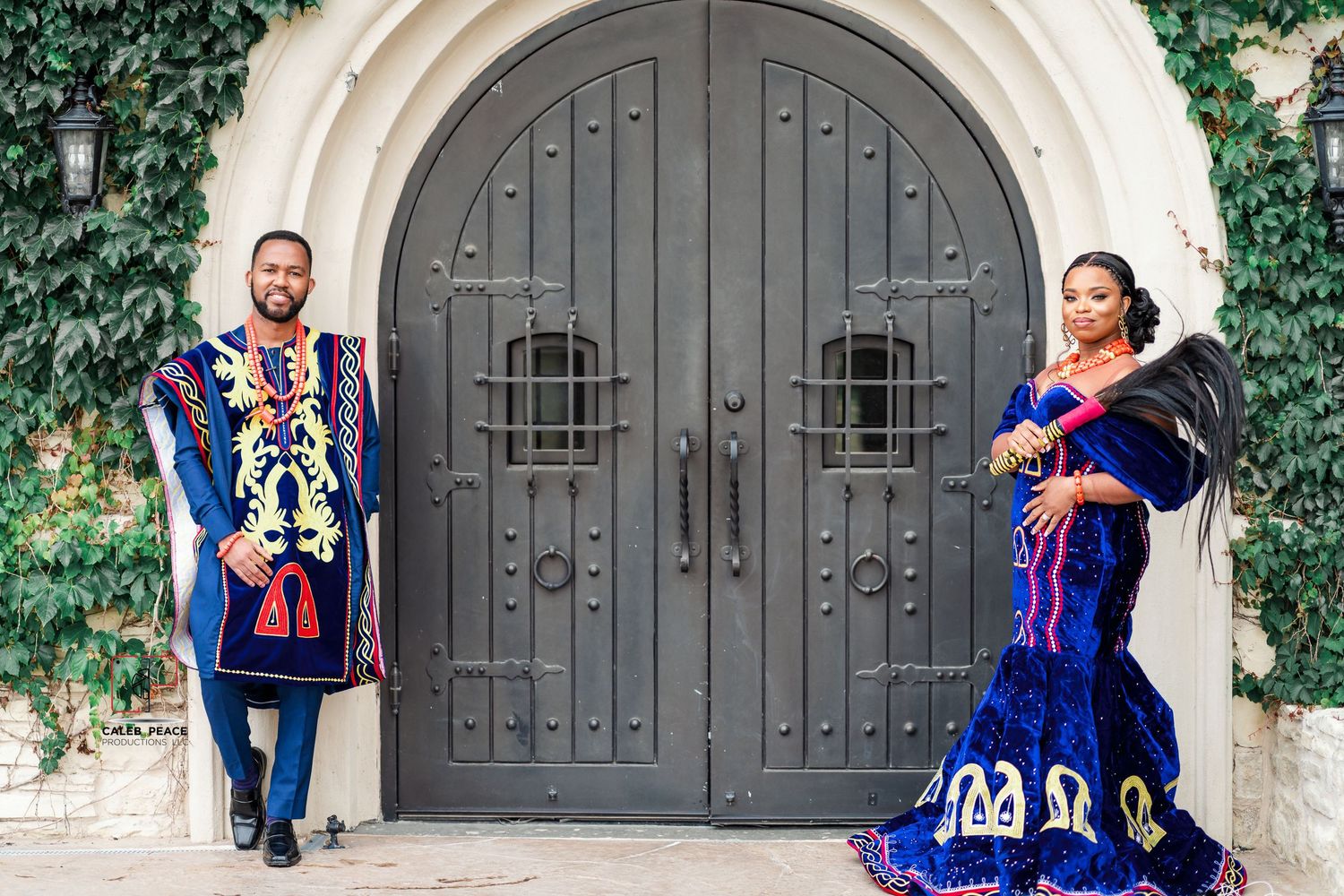 A couple in vibrant blue and red traditional Mexican attire poses together in front of an elegant stone archway.