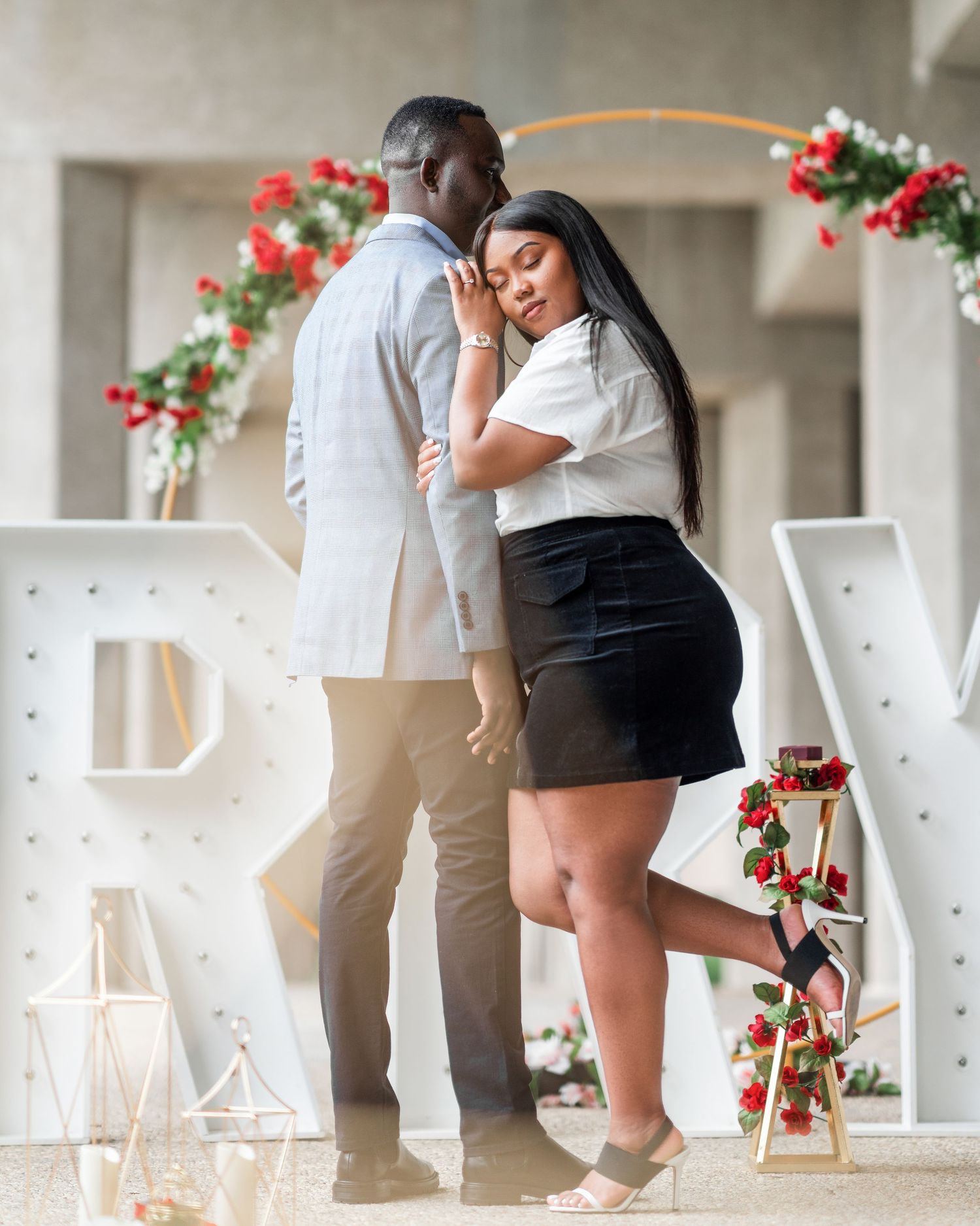 A couple in white and black outfits dancing together on a patio with red flowers in the background.