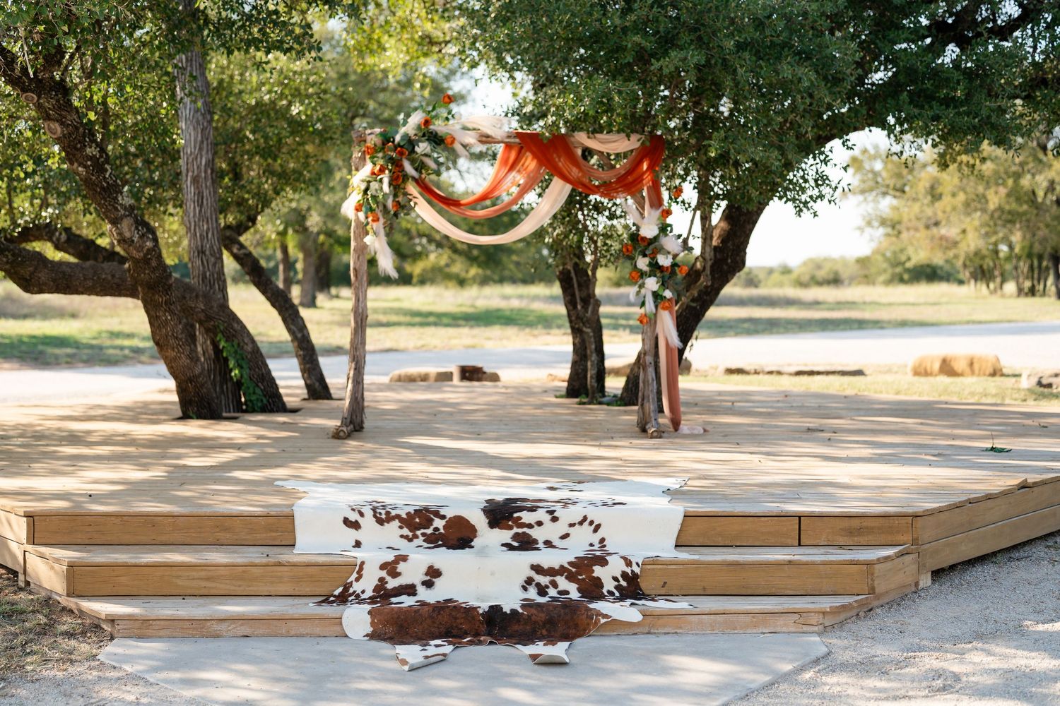 Outdoor wedding ceremony setup with wooden platform and red fabric draped between trees.