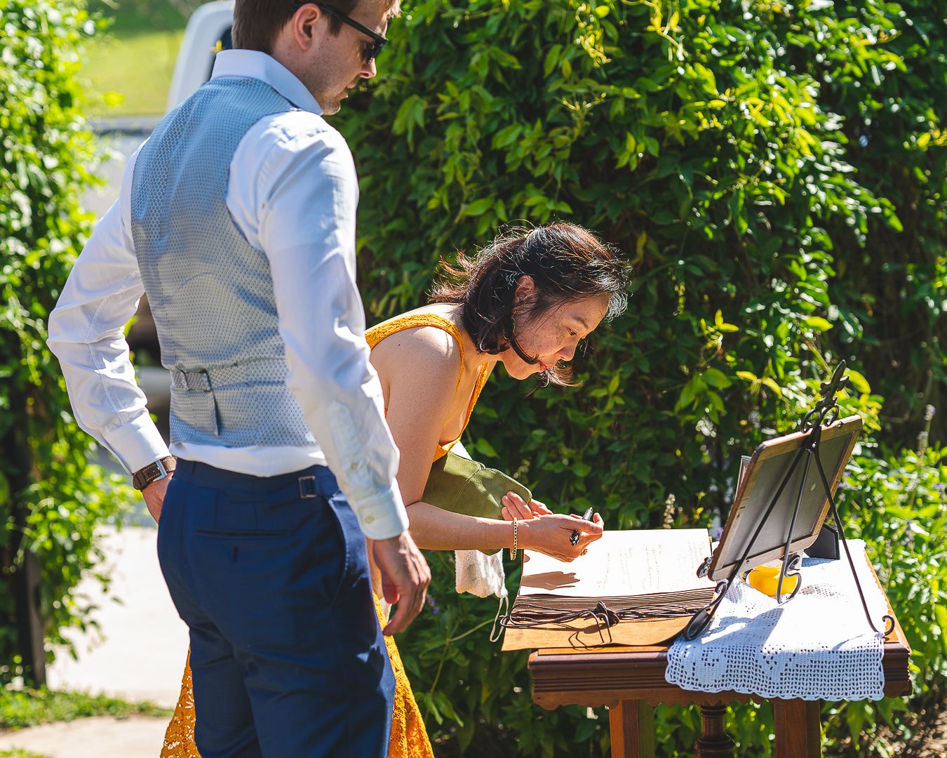 Wedding guests signing a guest book at an outdoor reception table.