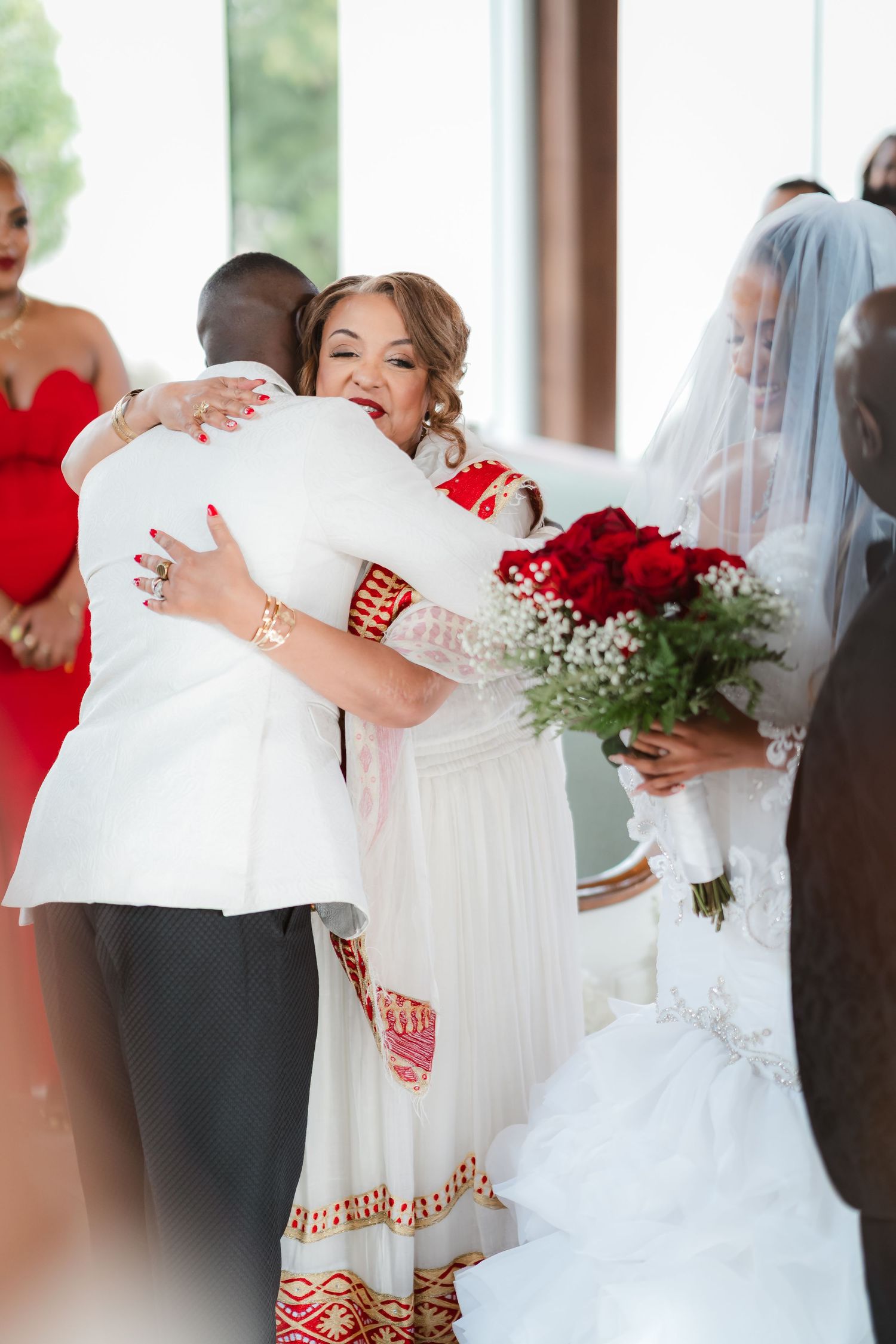 Wedding guests share warm embraces during a celebration decorated with red roses.