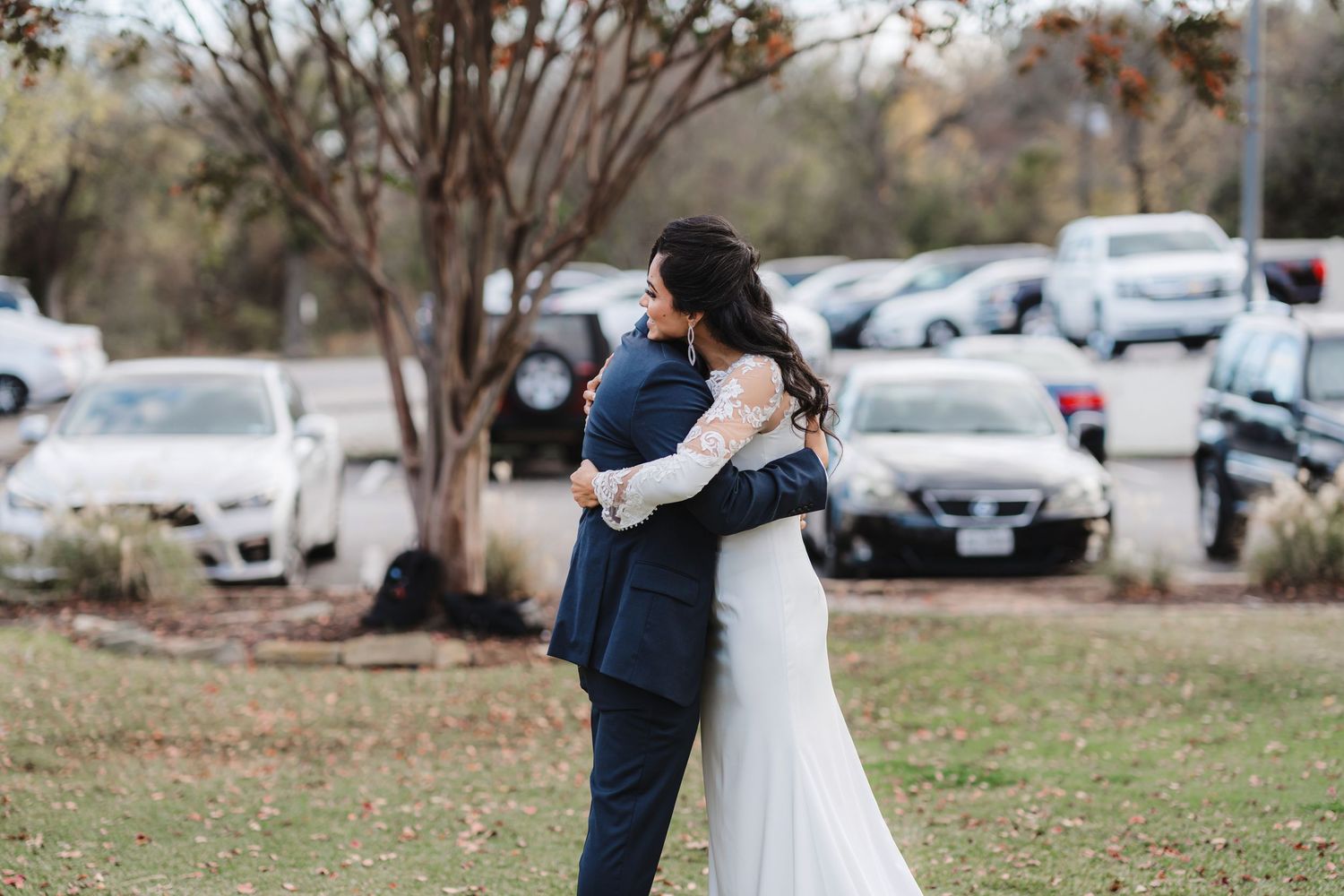 A couple shares romantic moments outdoors during their wedding photoshoot near parked cars.