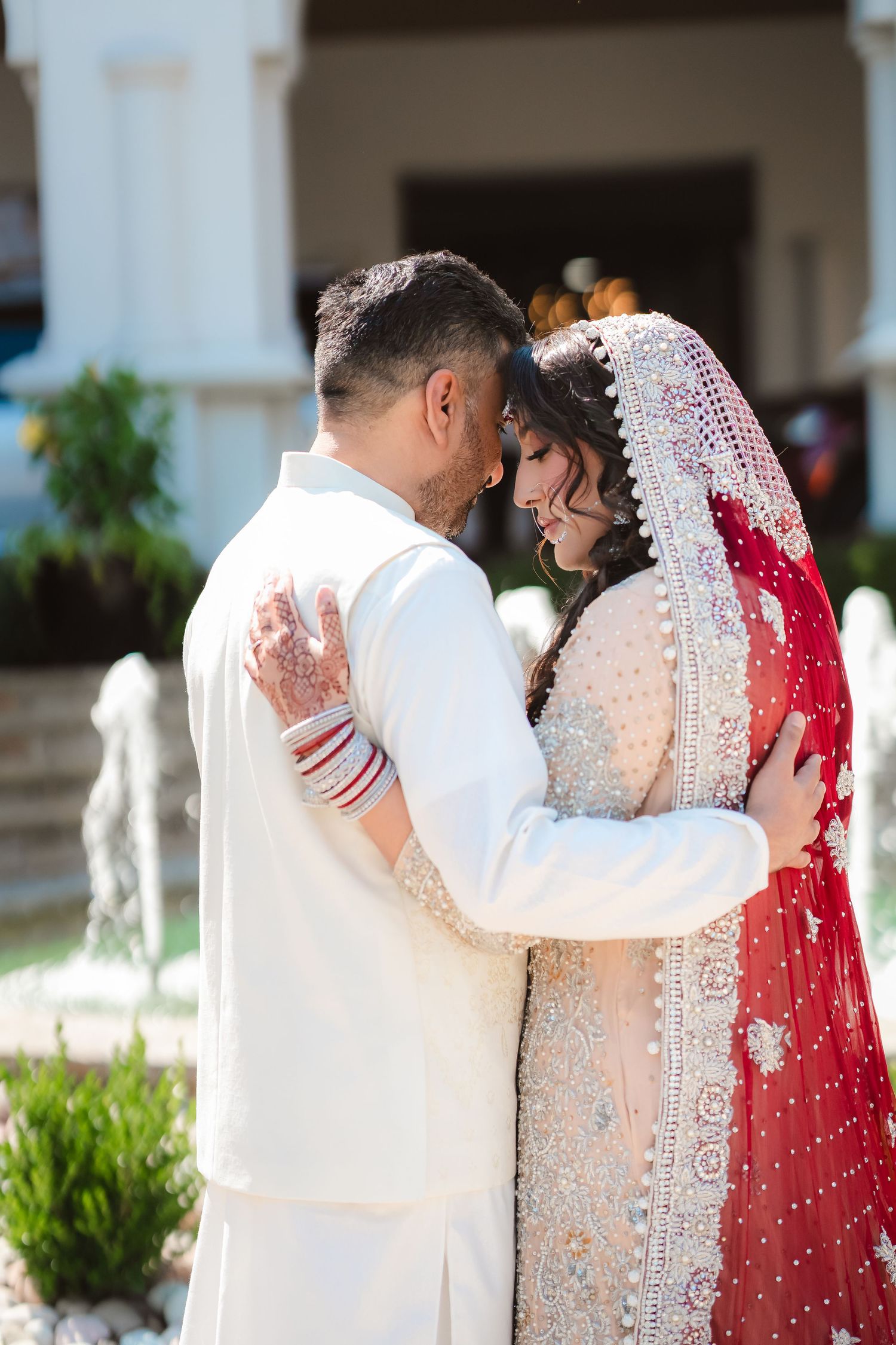 A romantic outdoor wedding moment showing traditional South Asian attire in white and red.
