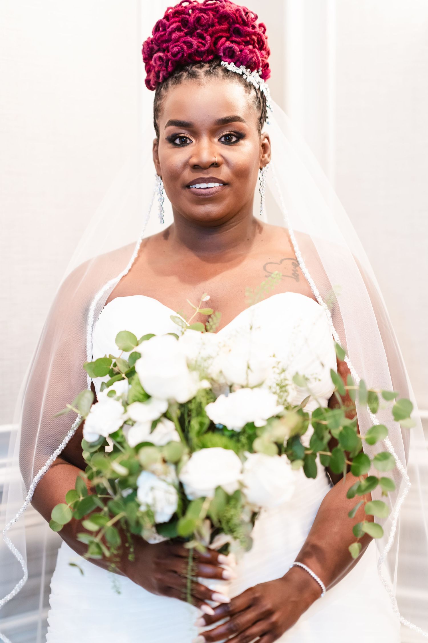 Bride in white dress holds beautiful white floral bouquet with eucalyptus against light background.