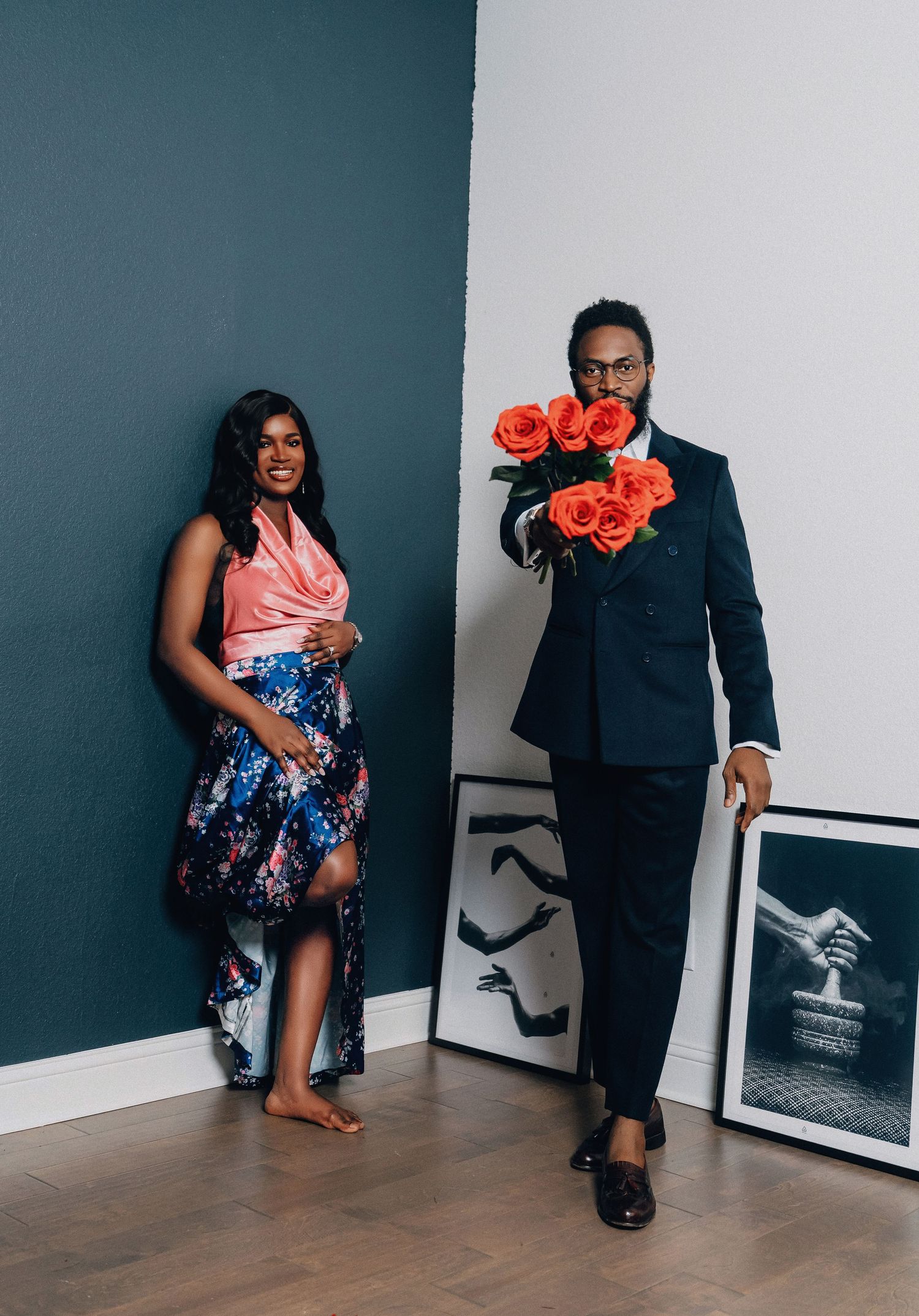 A couple posing with coral roses against a teal wall with black and white artwork.