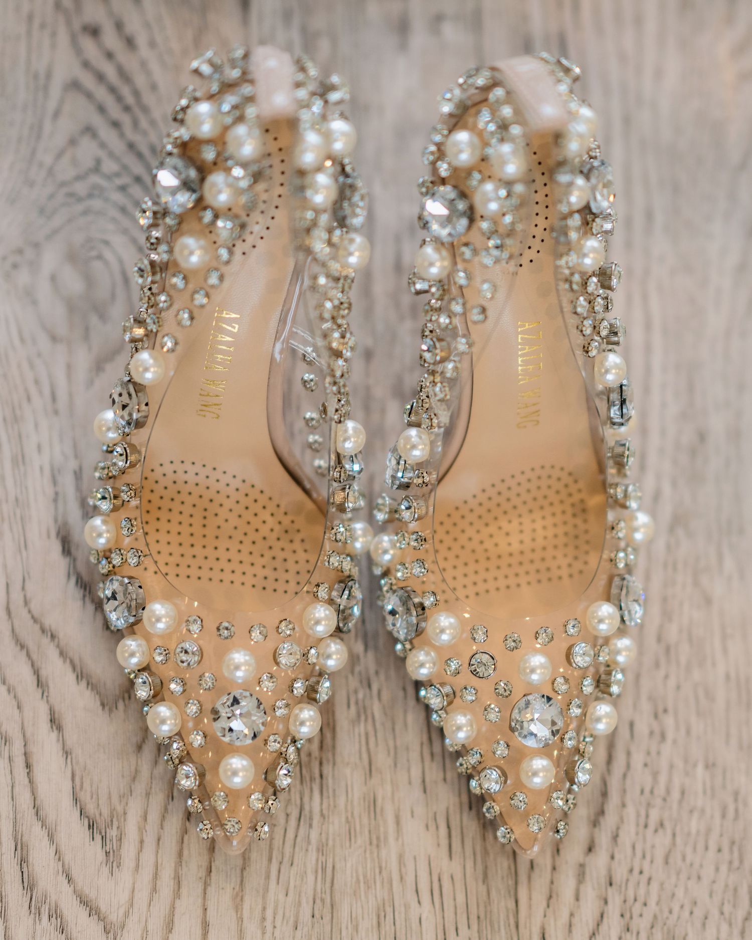Crystal and pearl embellished bridal shoes on a wooden surface.