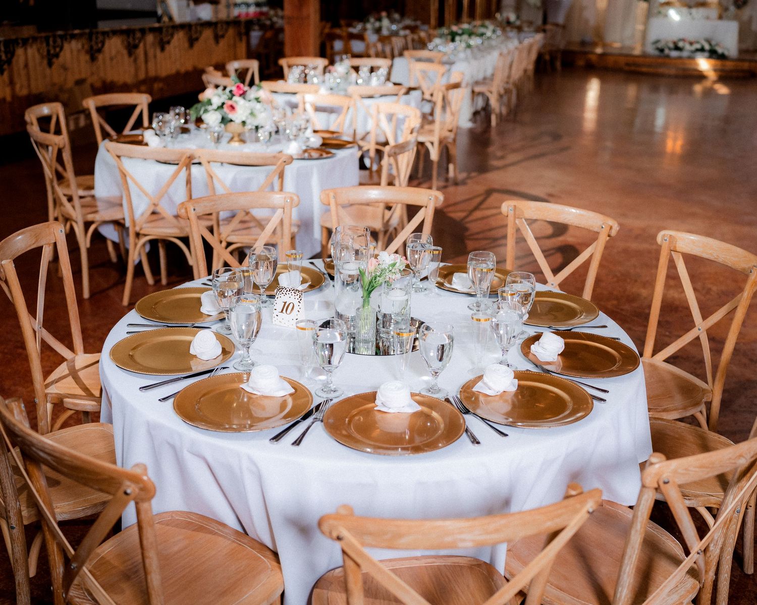 Elegant wedding reception setup with round tables, white linens, and wooden cross-back chairs in a rustic venue.