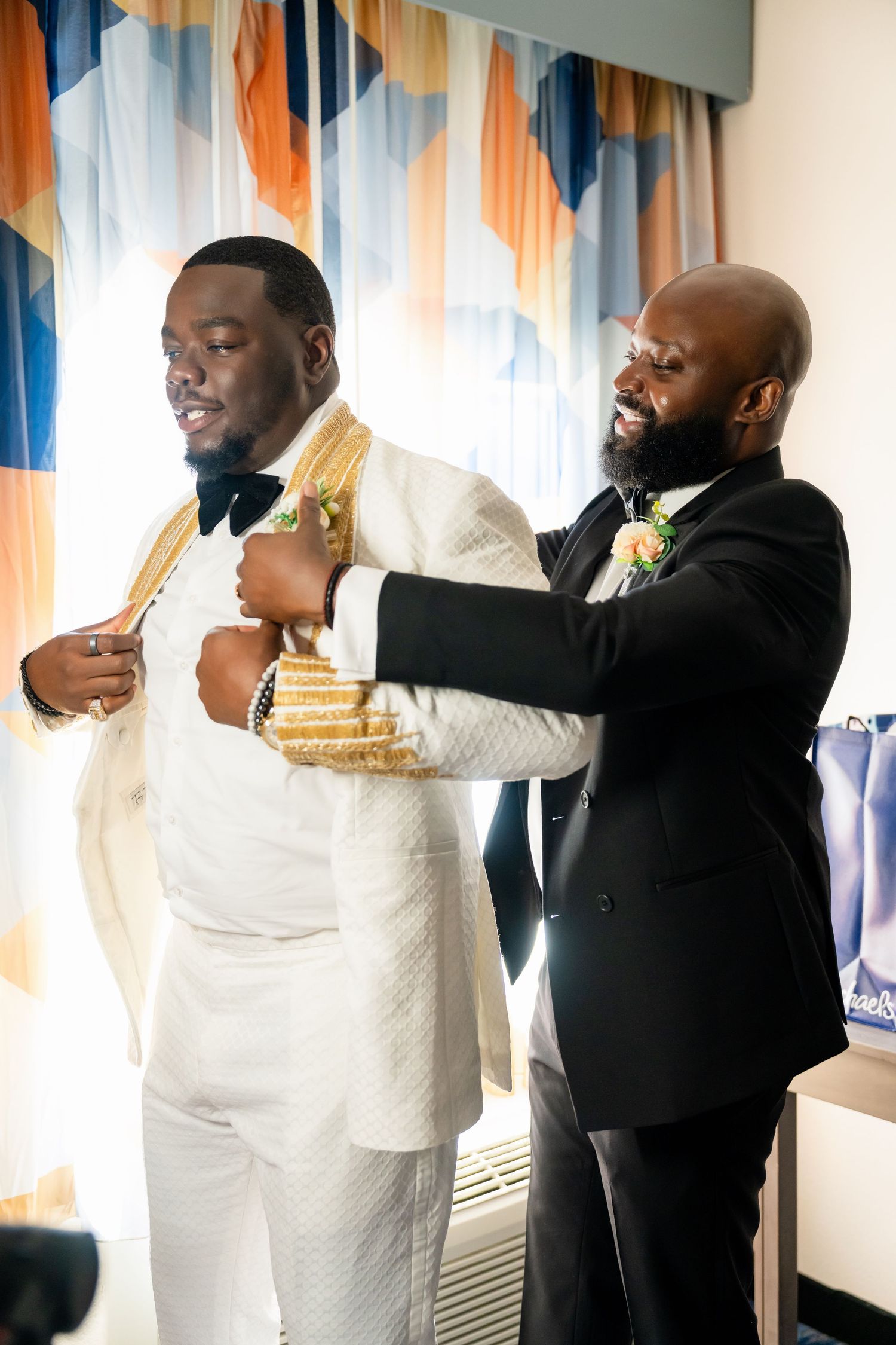 Groomsmen in black suits share emotional embraces during wedding celebration.