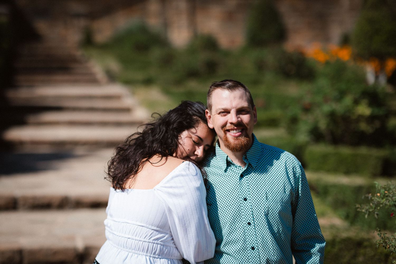 A couple shares a tender moment together while walking along stone steps in a lush garden setting.