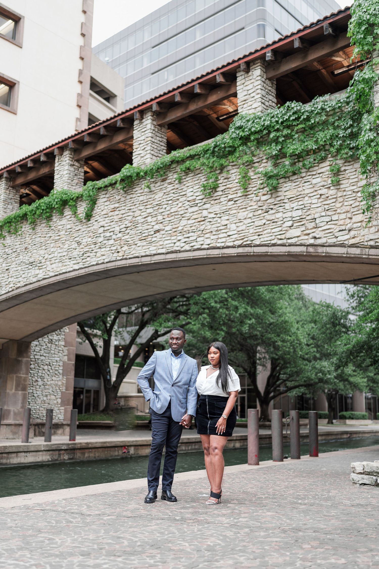 A couple shares a romantic moment under a stone archway along the San Antonio Riverwalk.