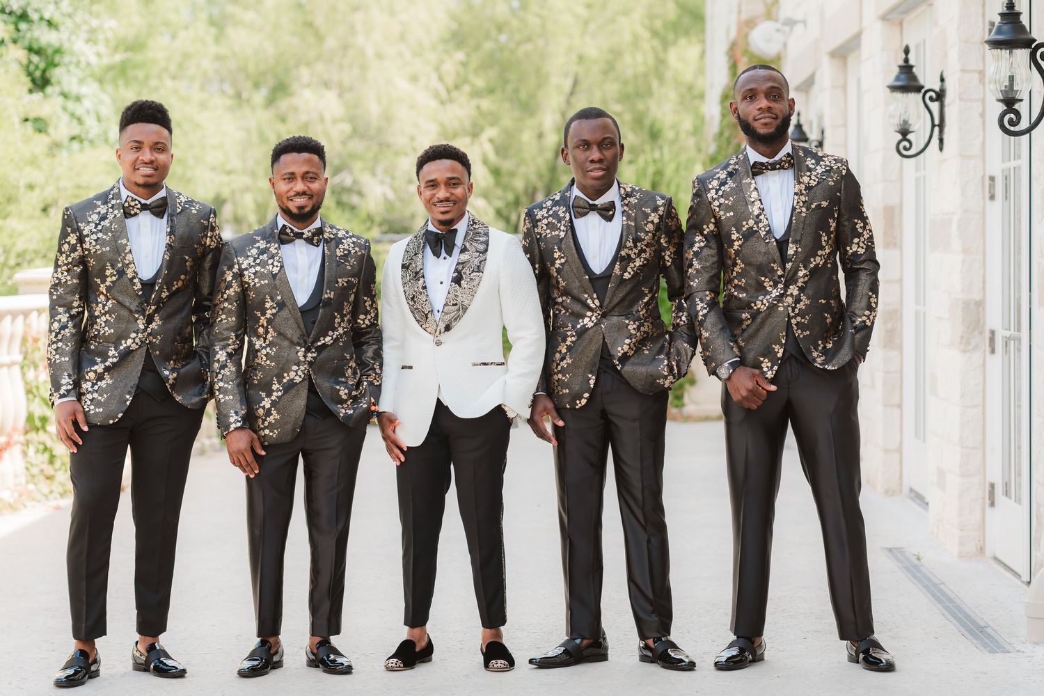 Groomsmen in matching floral print jackets and bow ties pose together outdoors.