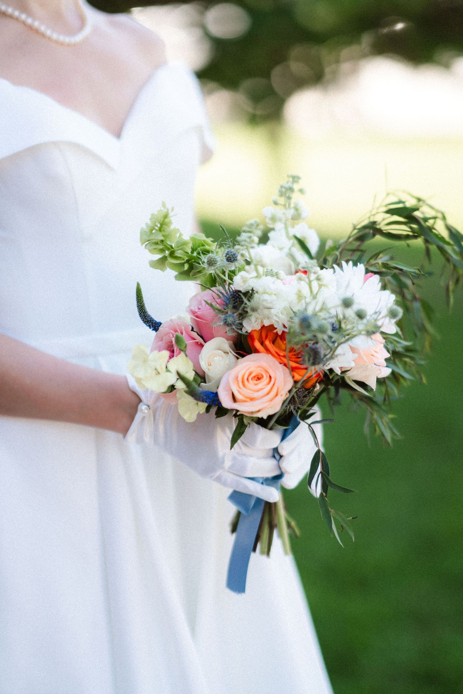 A bridal bouquet with pink roses, white flowers and greenery against a white wedding dress.