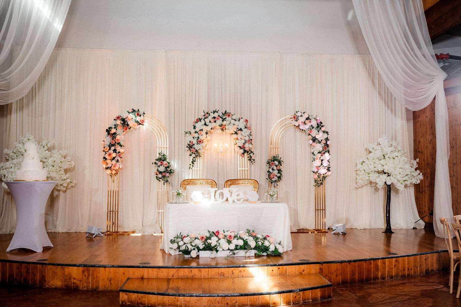 Wedding reception hall decorated with white draping, floral arrangements and elegant lighting.
