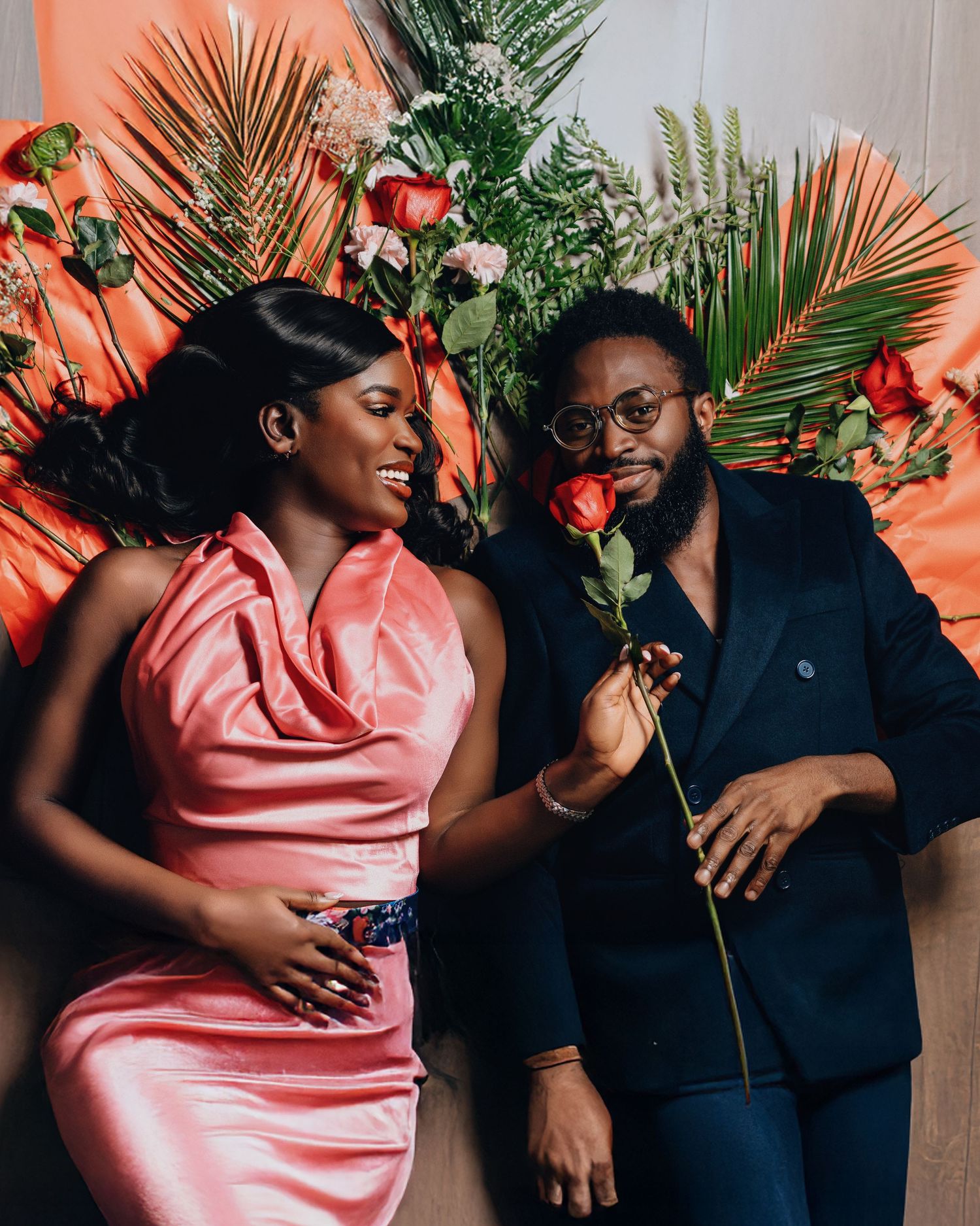 A couple shares a joyful moment surrounded by tropical palm leaves and coral-colored walls.