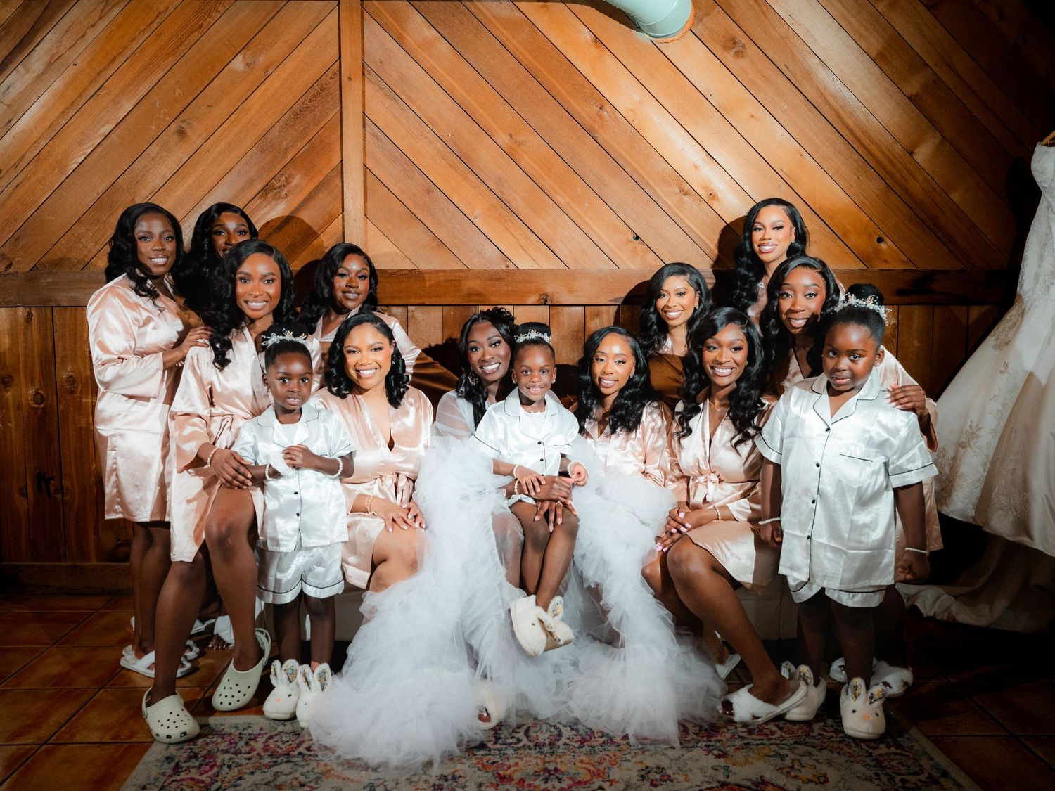 A bridal party in matching white robes poses together in a rustic wooden venue.