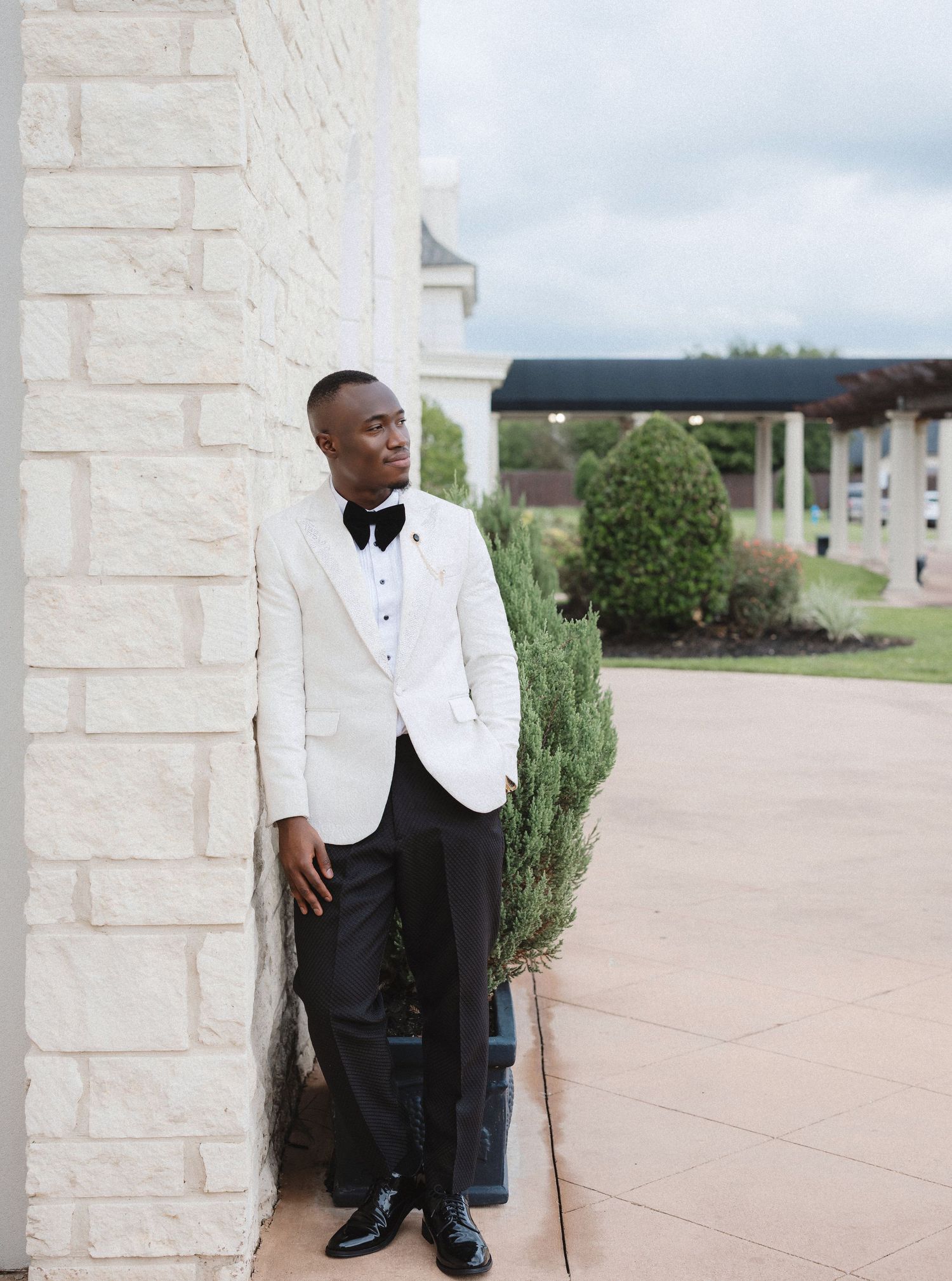 Formal portrait session against white stone columns and landscaping in classic black and white attire.