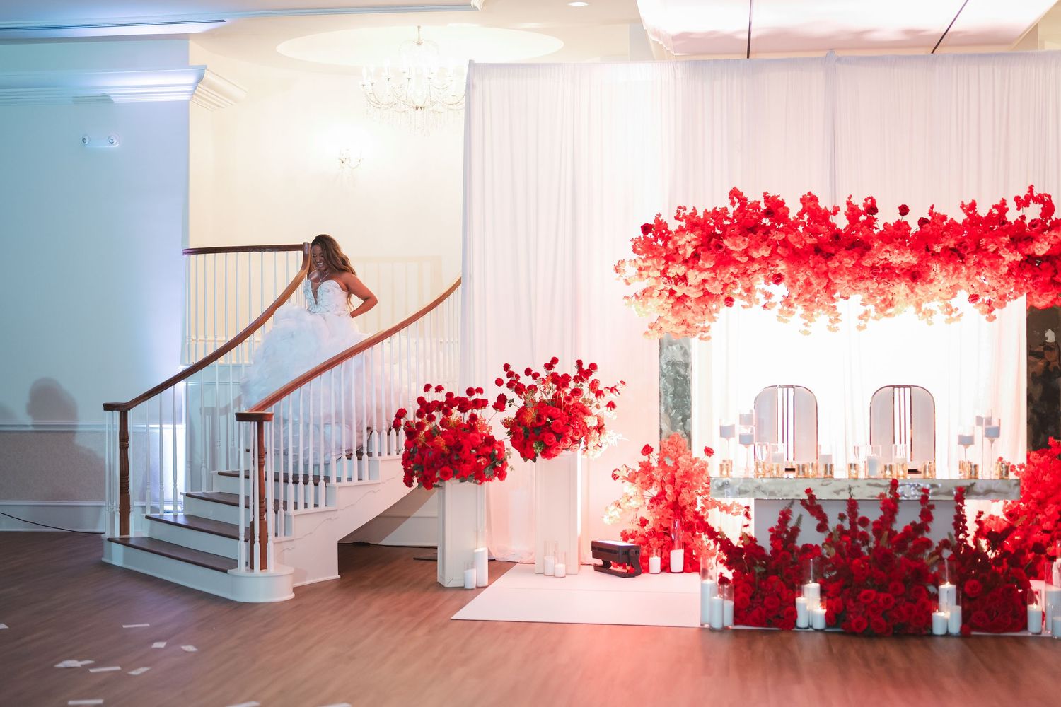 Wedding venue interior decorated with dramatic red floral installations and white drapery.
