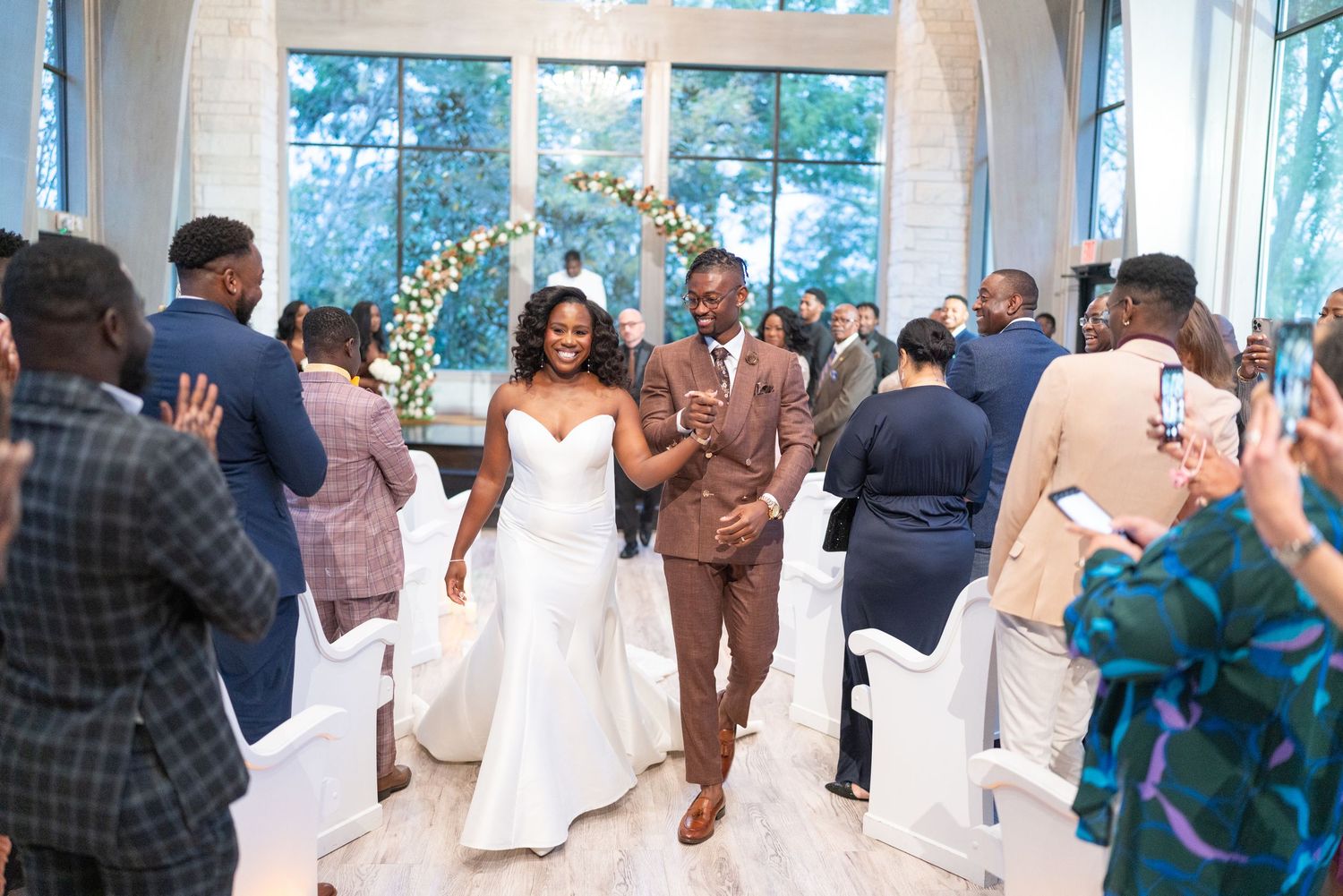 Wedding reception celebration with guests dancing and enjoying festivities in a bright venue with large windows.