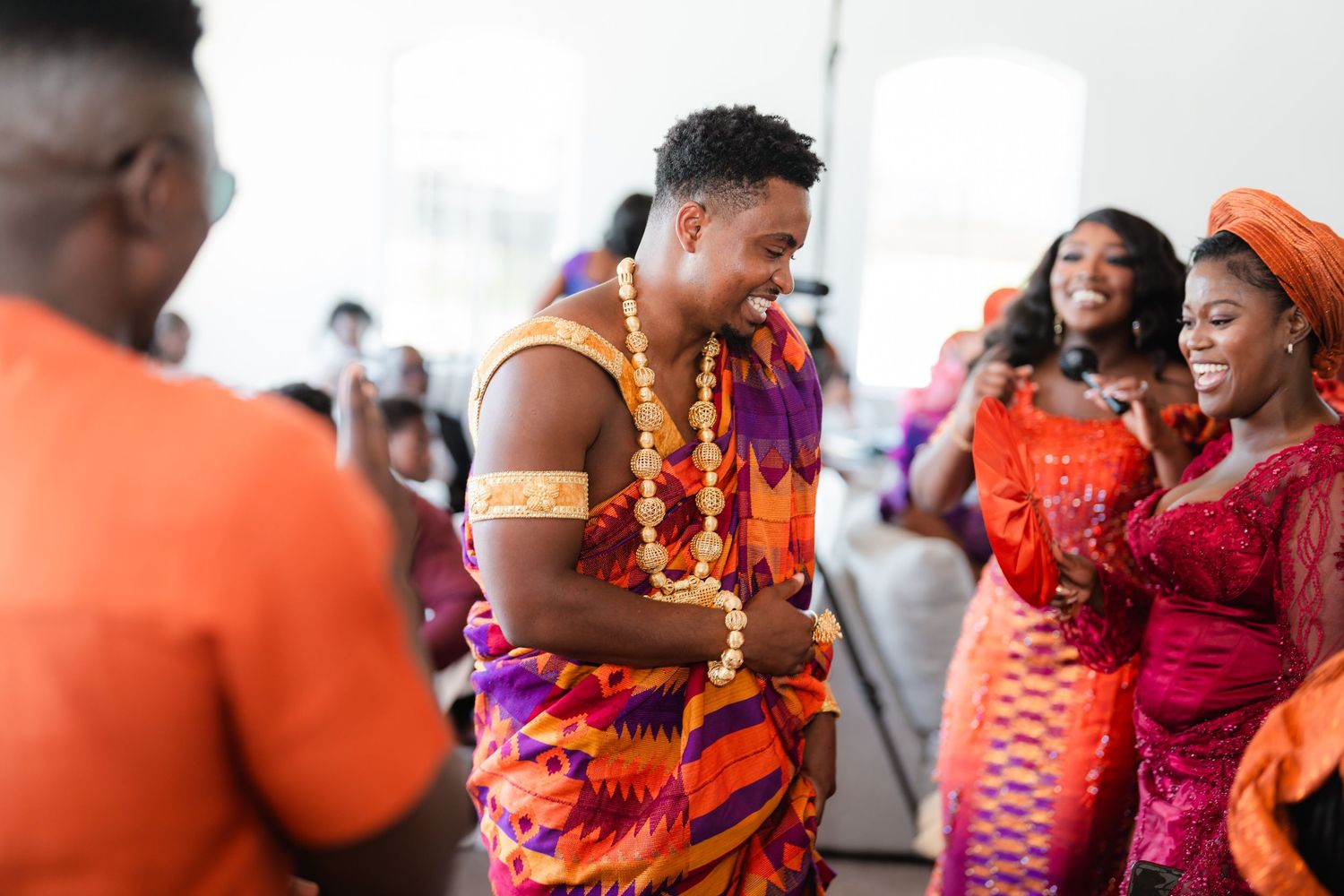 Guests in colorful traditional African attire celebrate and dance during a festive gathering.